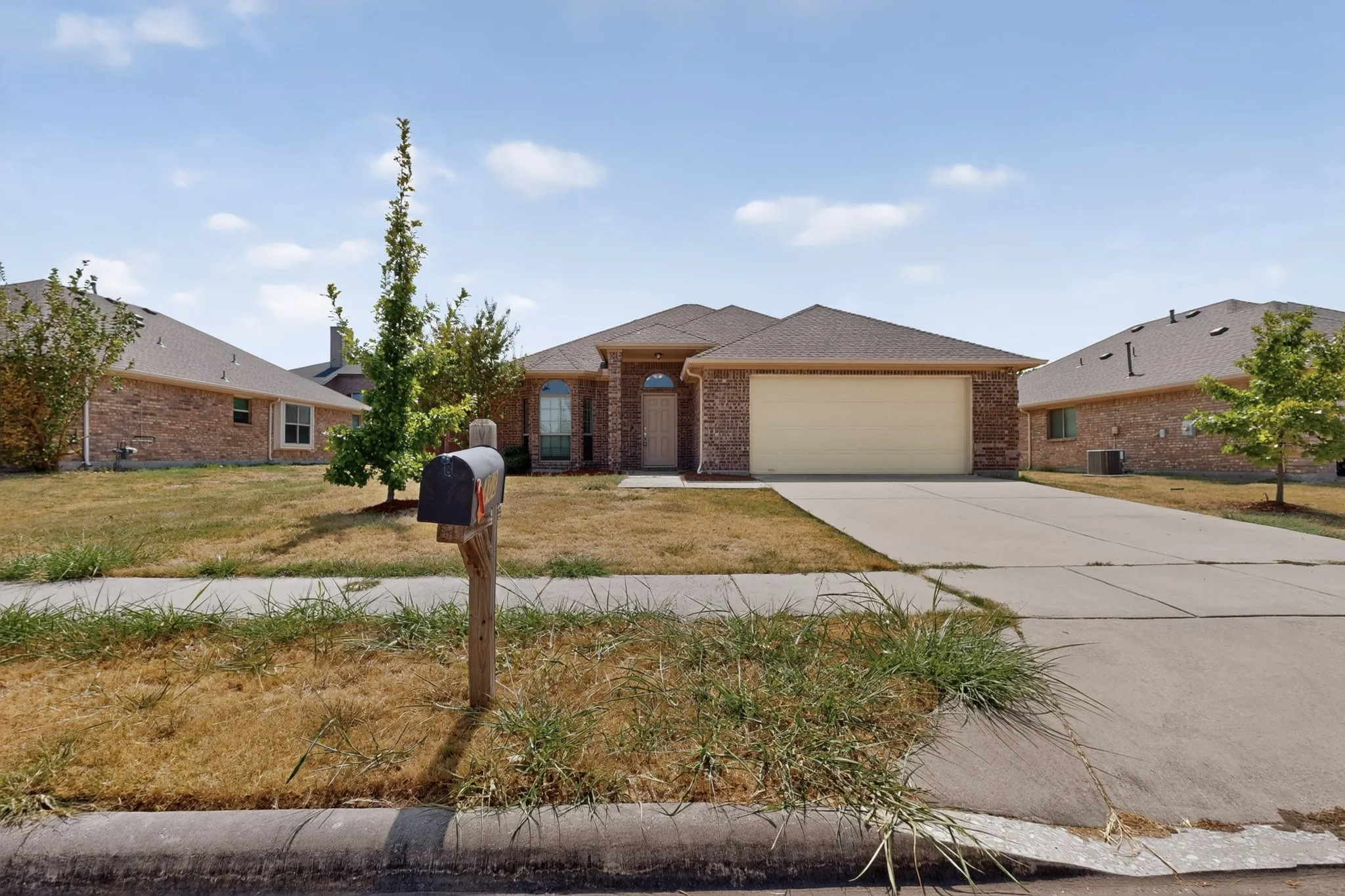 Brick exterior with an attached two-car garage, concrete driveway, and a front yard