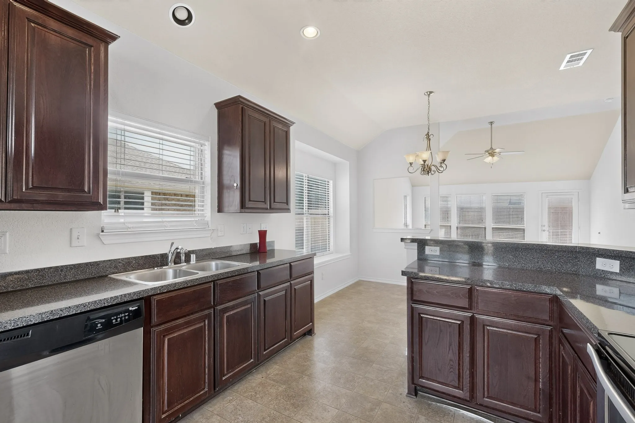 Kitchen featuring dark wood-finish cabinetry, dark countertops, a double basin stainless steel sink, and stainless steel dishwasher