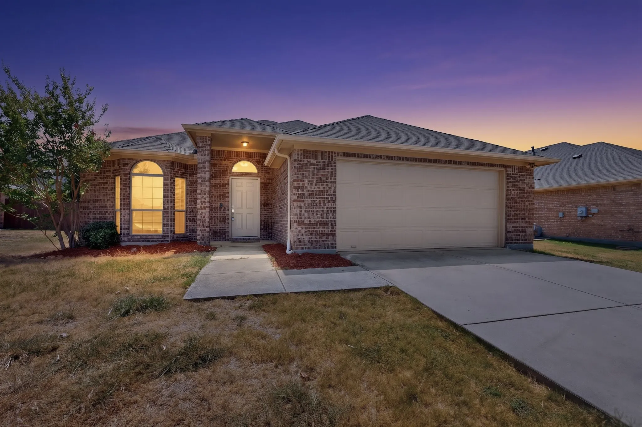 Brick exterior with arch-top windows, an attached garage, and concrete pathways