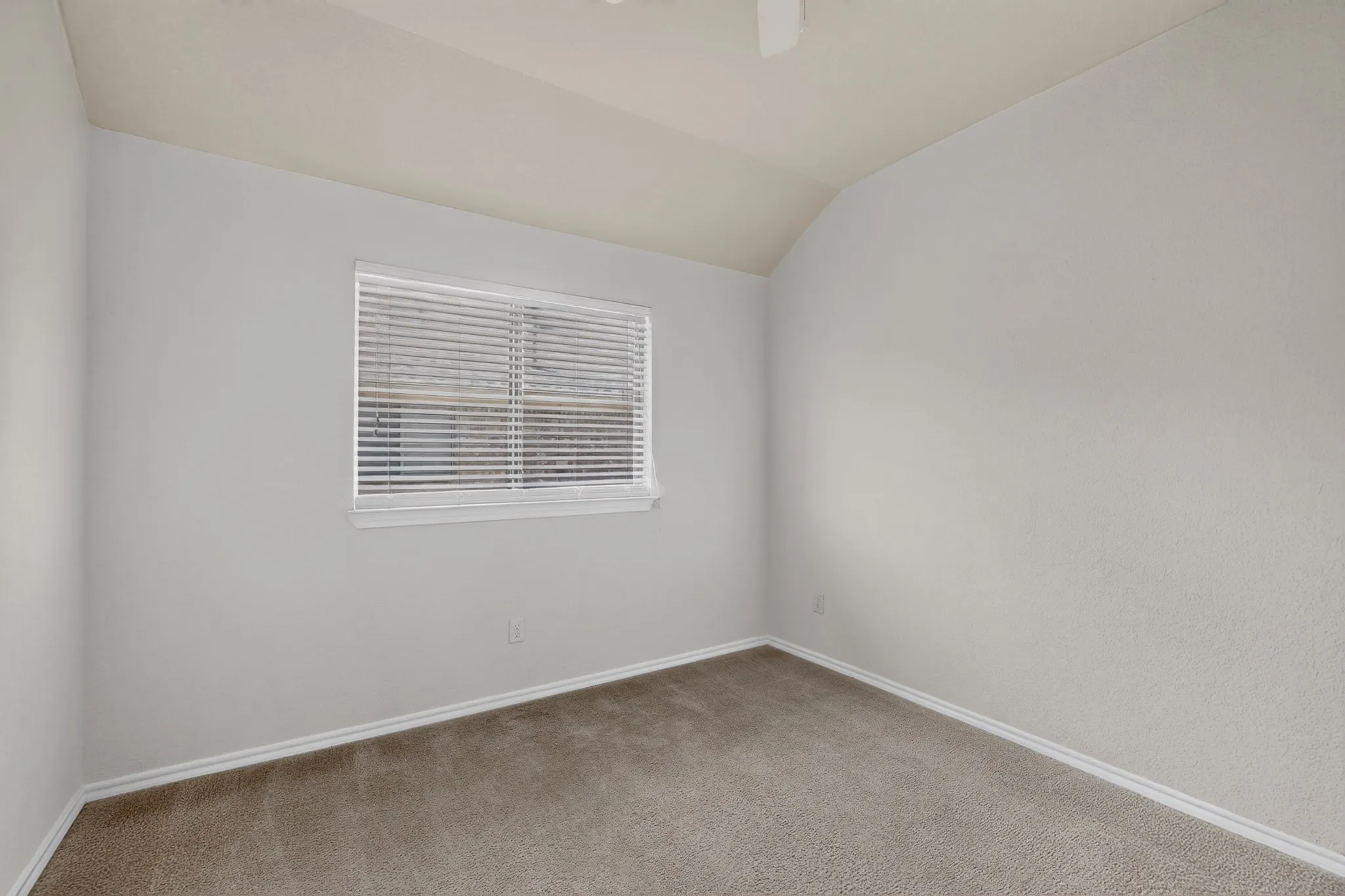 Sloped ceiling with an attached ceiling fan, window with horizontal blinds, and carpeted flooring