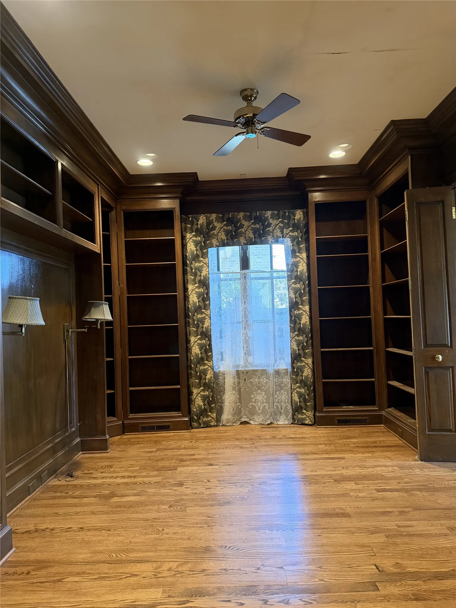 Paneled library with bookshelves surrounding and hardwood floors.