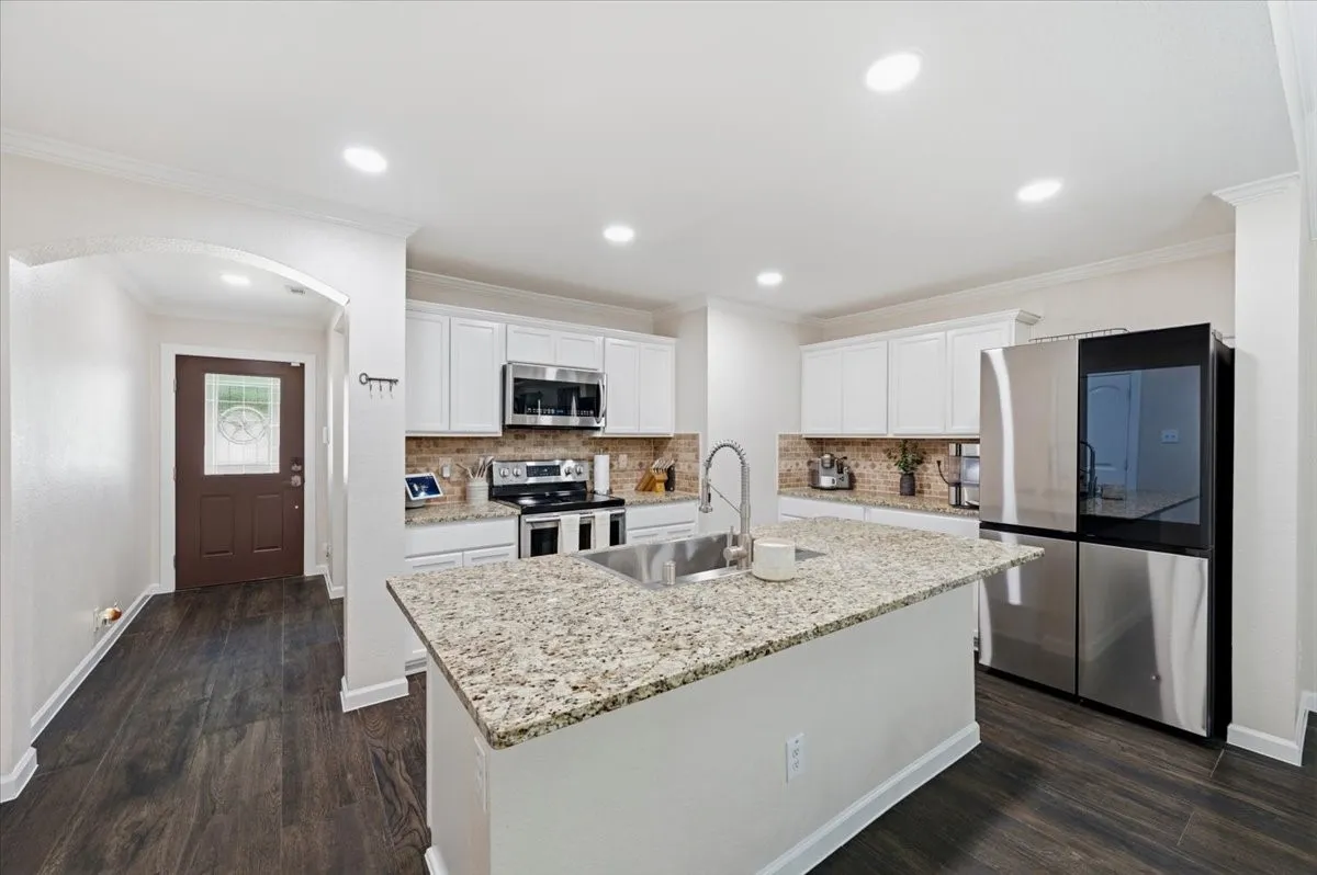 Kitchen featuring an island with a stainless steel sink, granite countertops, white cabinetry, and stainless steel​​‌​​​​‌​​‌‌​‌‌​​​‌‌​‌​‌​‌​​​‌​​ appliances