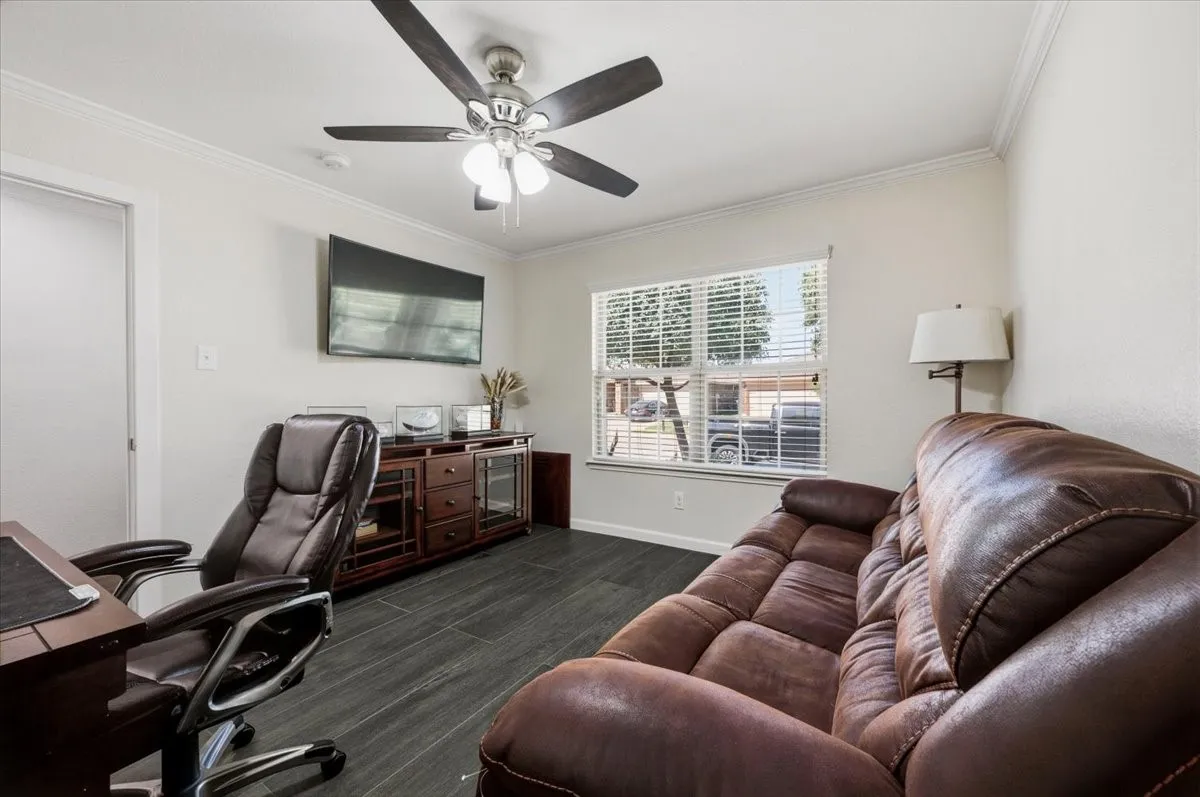 White crown molding, dark wood-finish flooring, a ceiling fan with integrated lighting, and a large window with horizontal blinds