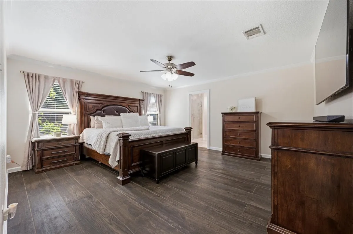 Spacious room featuring wood-finish flooring, a ceiling fan, crown molding, and multiple windows