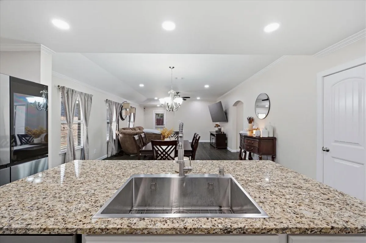 Kitchen island with a stainless steel undermount sink, speckled countertop, and recessed lighting
