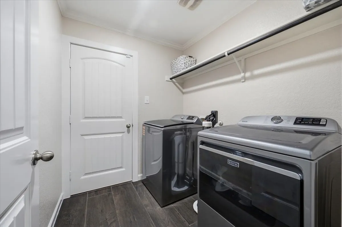 Laundry area featuring dark wood-finish flooring, white walls, overhead shelving, and a white interior door with an arched panel design