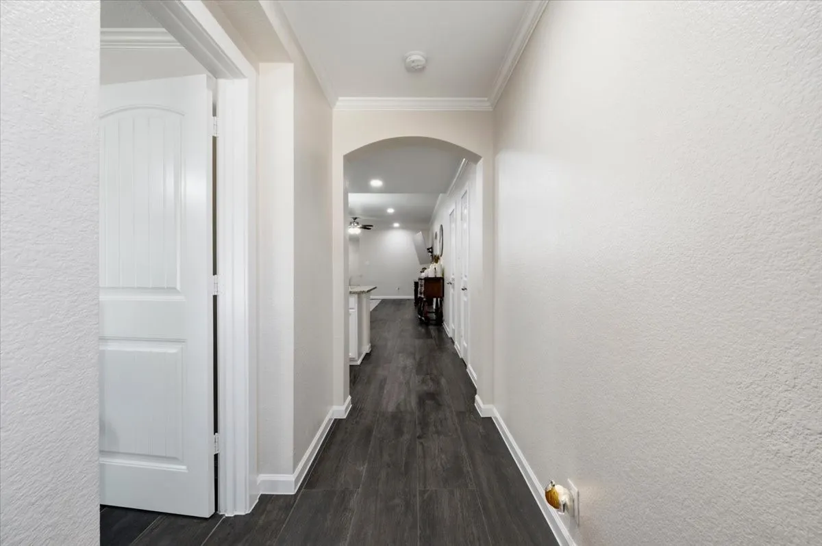 Hallway featuring wood-finish flooring, an arched entryway, and white trim