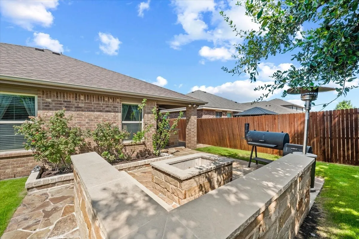Expansive backyard featuring a stone-clad fire pit, integrated stone seating, and a large grassy area