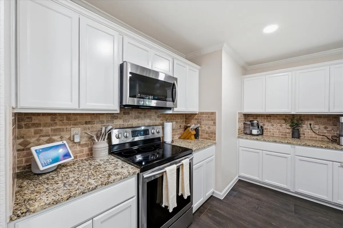 Kitchen featuring white cabinetry, granite countertops, stainless steel appliances, brick-patterned backsplash, and wood-finish flooring
