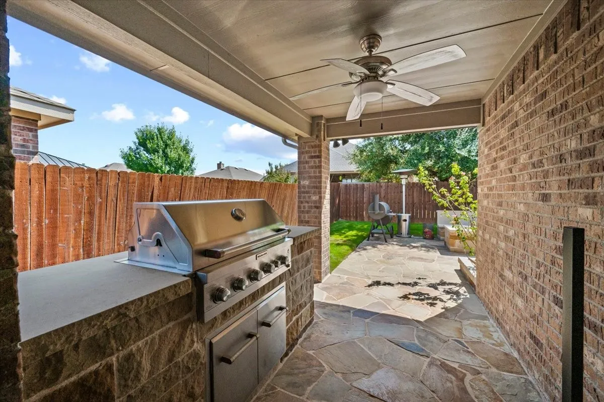 Covered patio featuring a built-in outdoor grill, stone-finish counter, and a ceiling fan