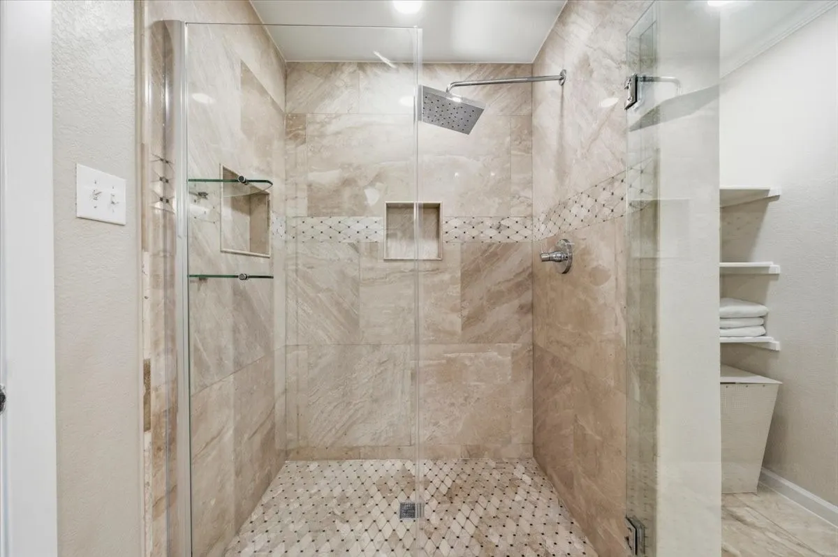 Glass-enclosed shower with large format wall tile, mosaic floor tile, built-in shower niches, and a rainfall showerhead