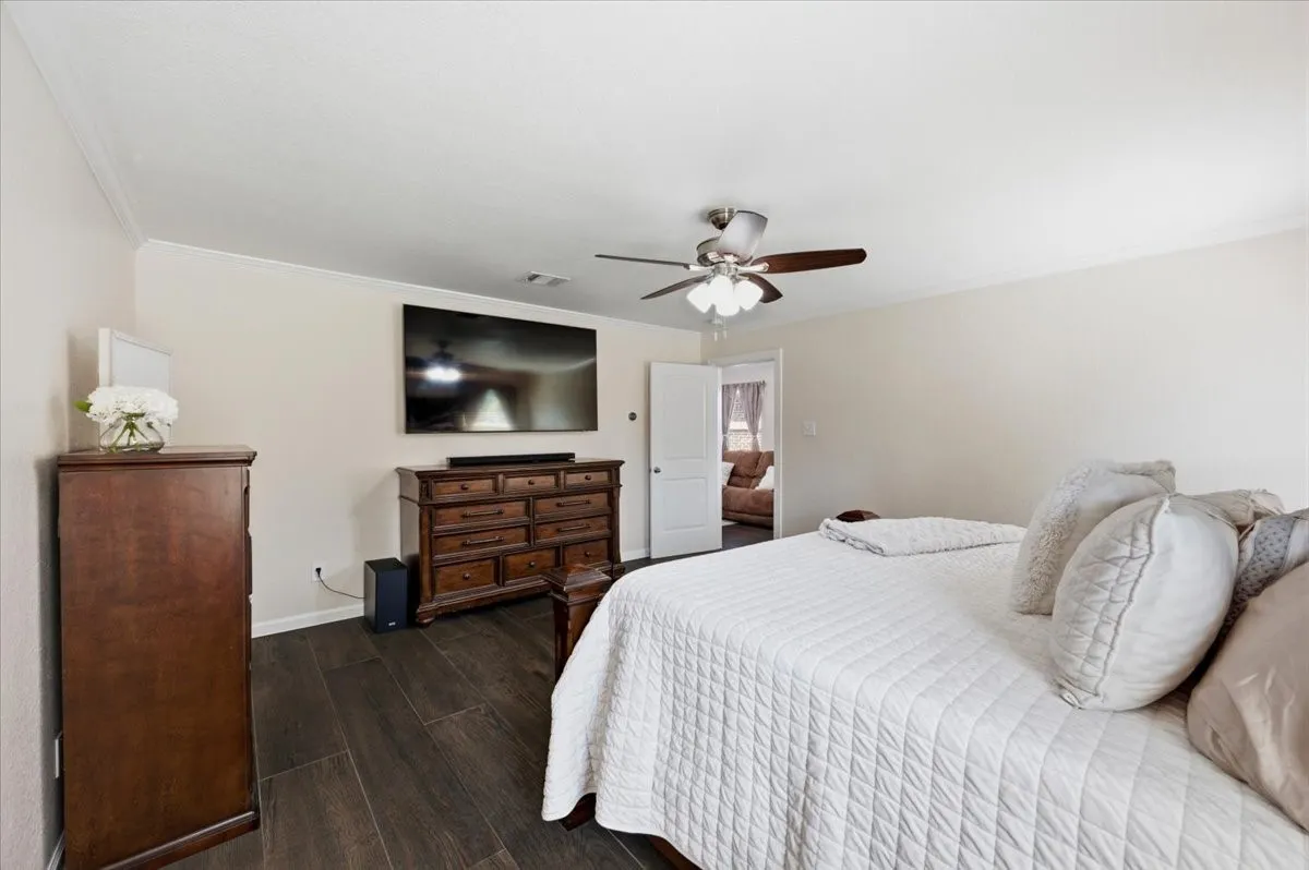 Wood-finish flooring, crown molding, and a ceiling fan with light fixture