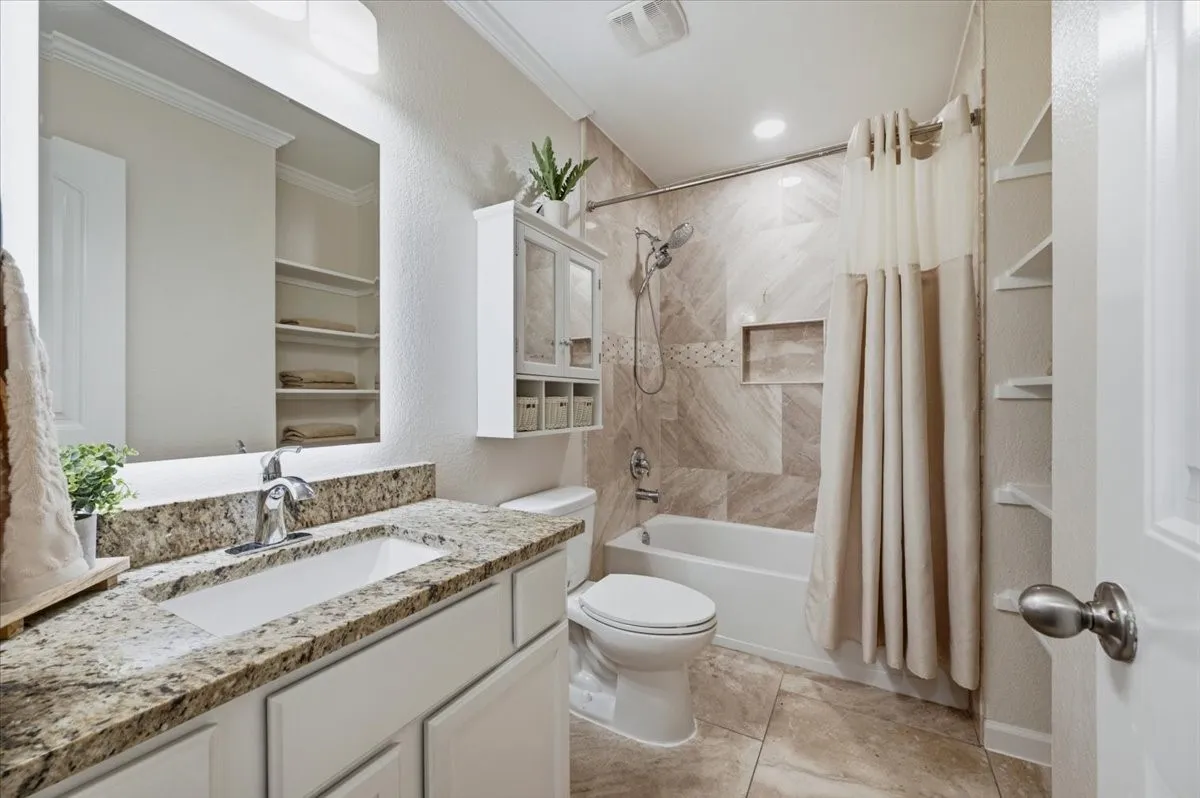 Bathroom featuring a vanity with a rectangular undermount sink, granite countertop, built-in shelving, and a tiled tub/shower combination with a recessed niche