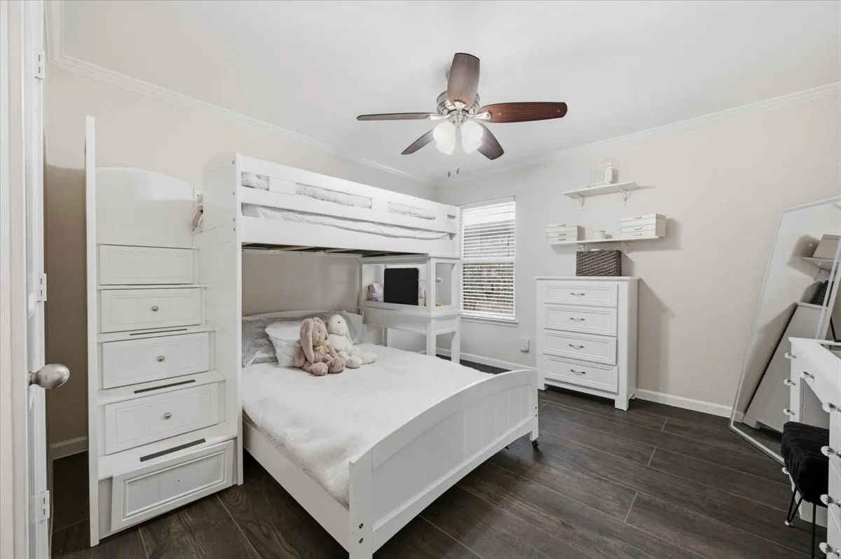 Dark wood-finish flooring, crown molding, ceiling fan with integrated lighting, and a window with horizontal blinds