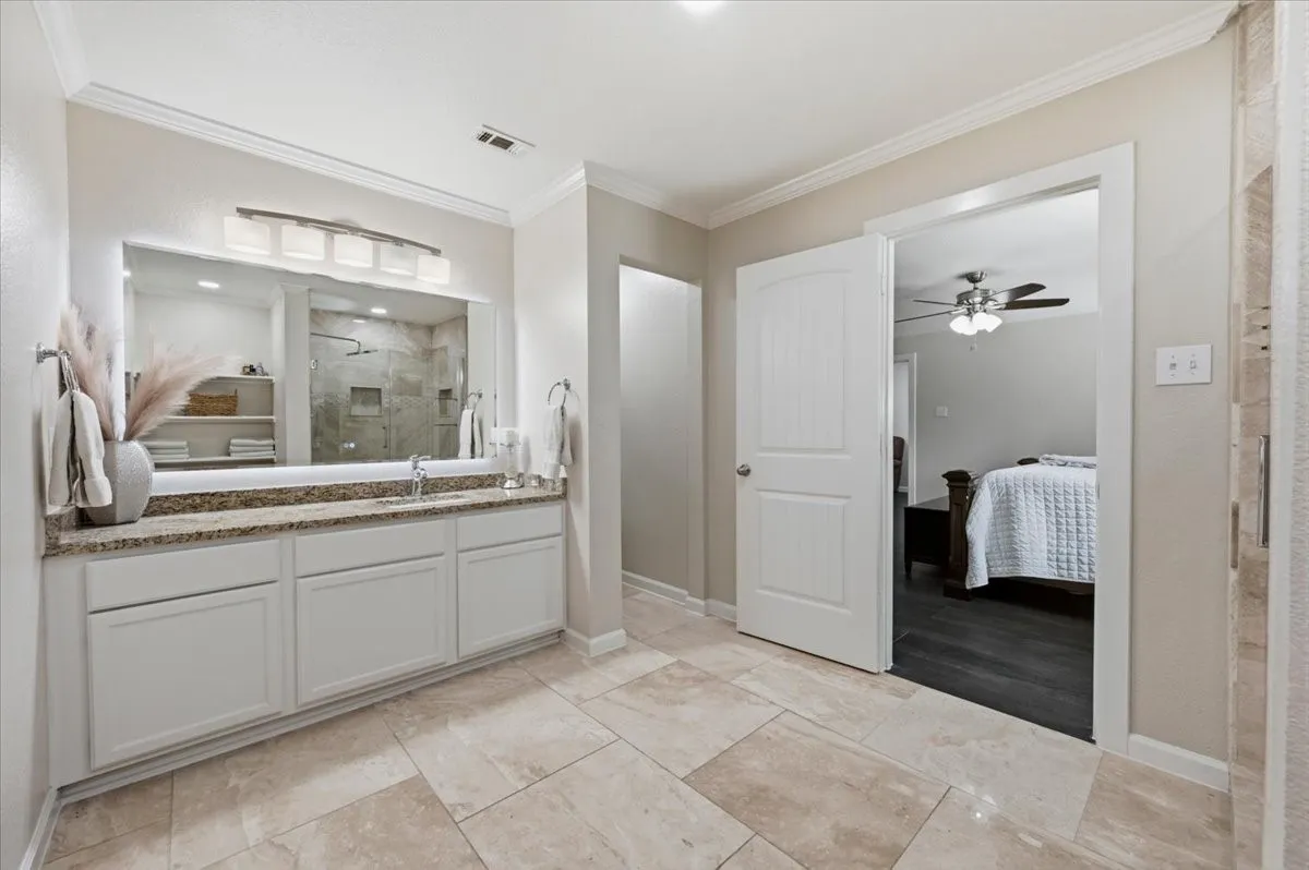 Double vanity with a stone countertop, white cabinetry, and a large illuminated mirror