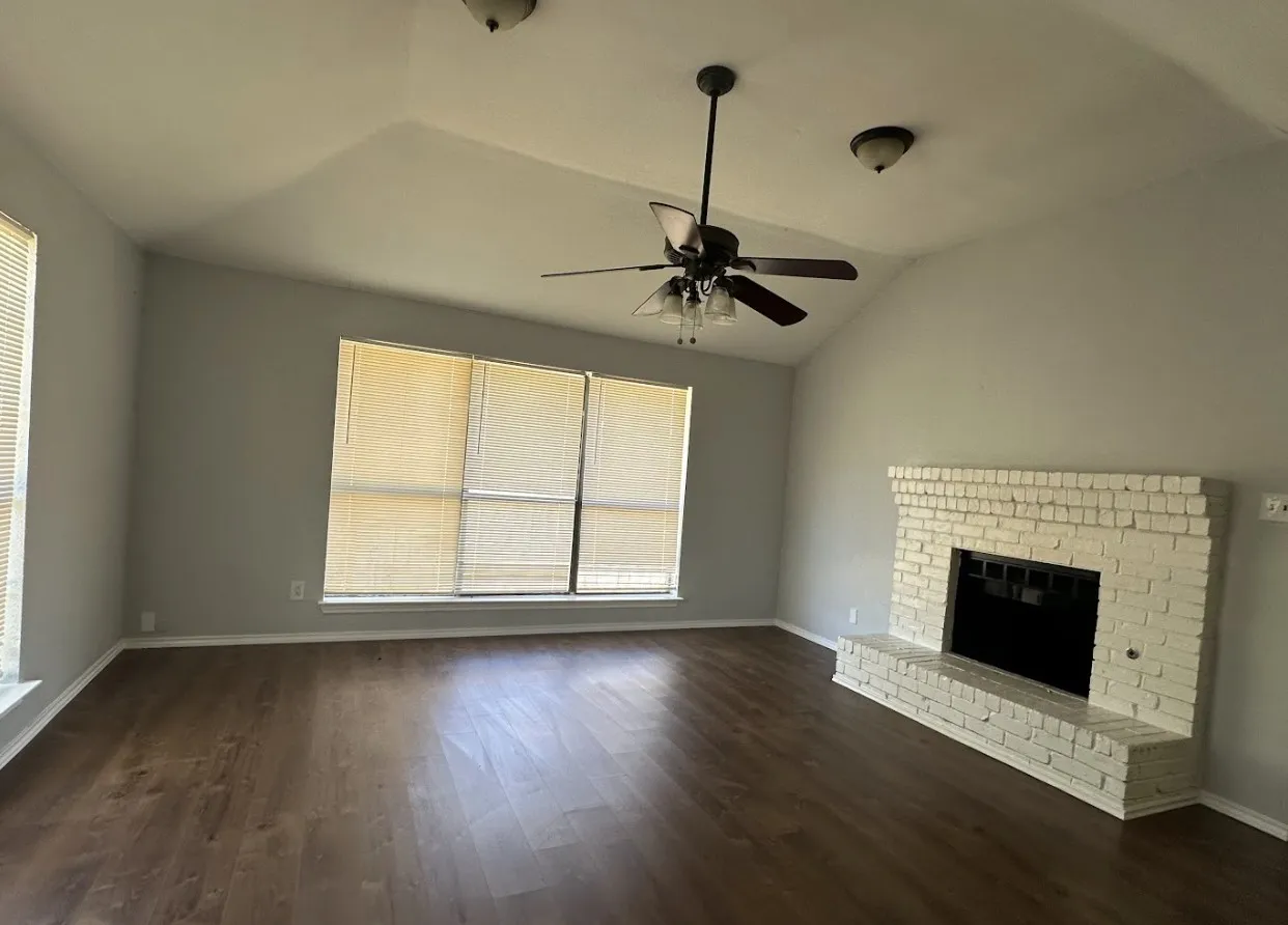 Vaulted ceiling with a ceiling fan, wood-finish flooring, and a painted brick fireplace