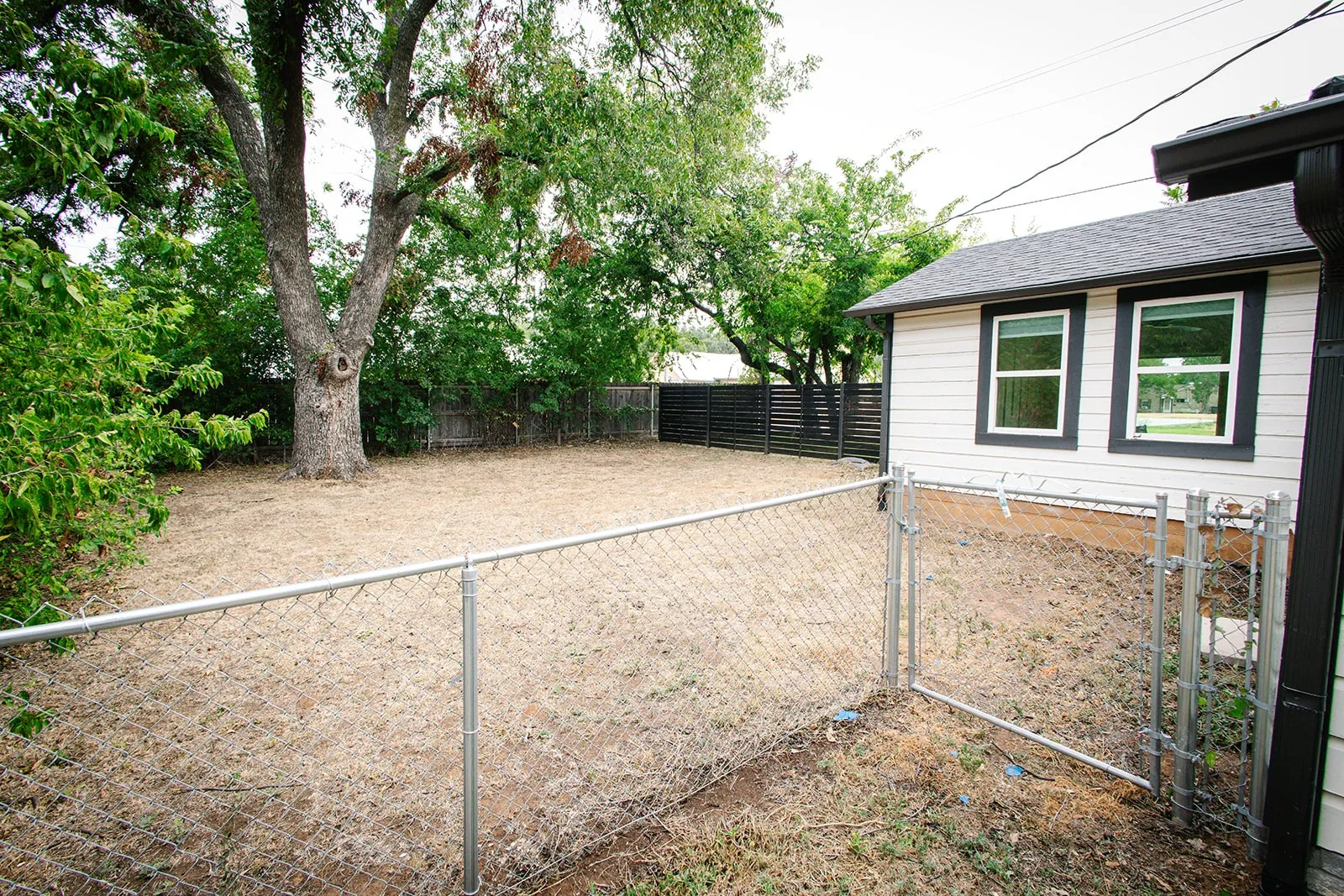 Separate fenced area Expansive backyard featuring a mature tree, chain-link fencing, and a dark slat fence