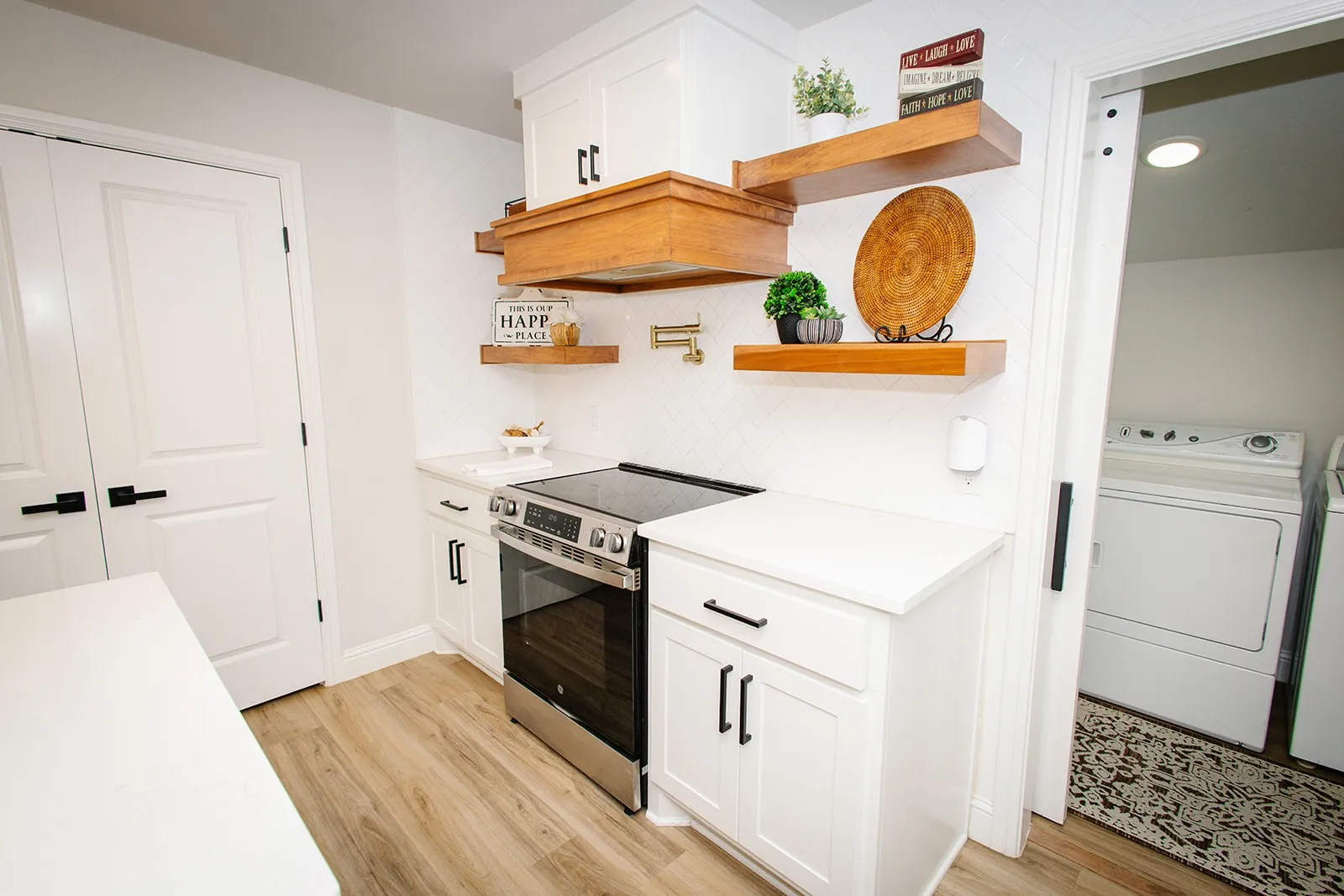 White cabinetry with black hardware, wood-finish flooring, stainless steel range, white countertops, and wood floating shelves