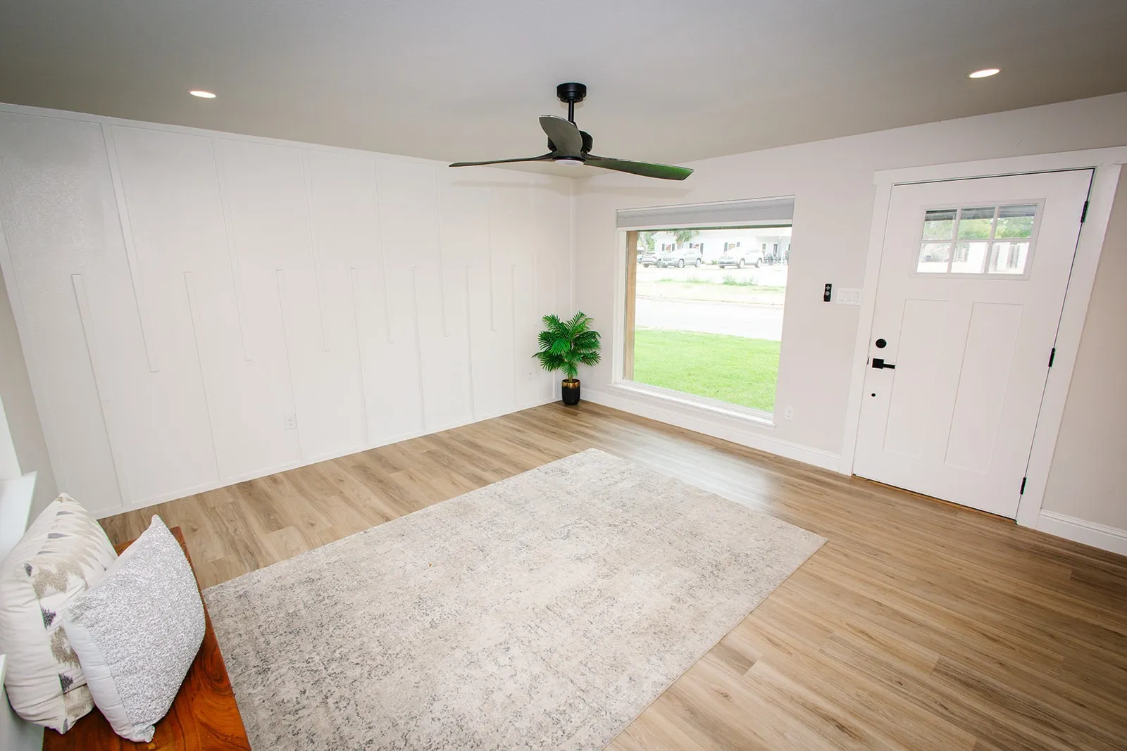 Wood-finish flooring, white paneled accent wall, recessed lighting, modern ceiling fan, and white entry door with frosted glass