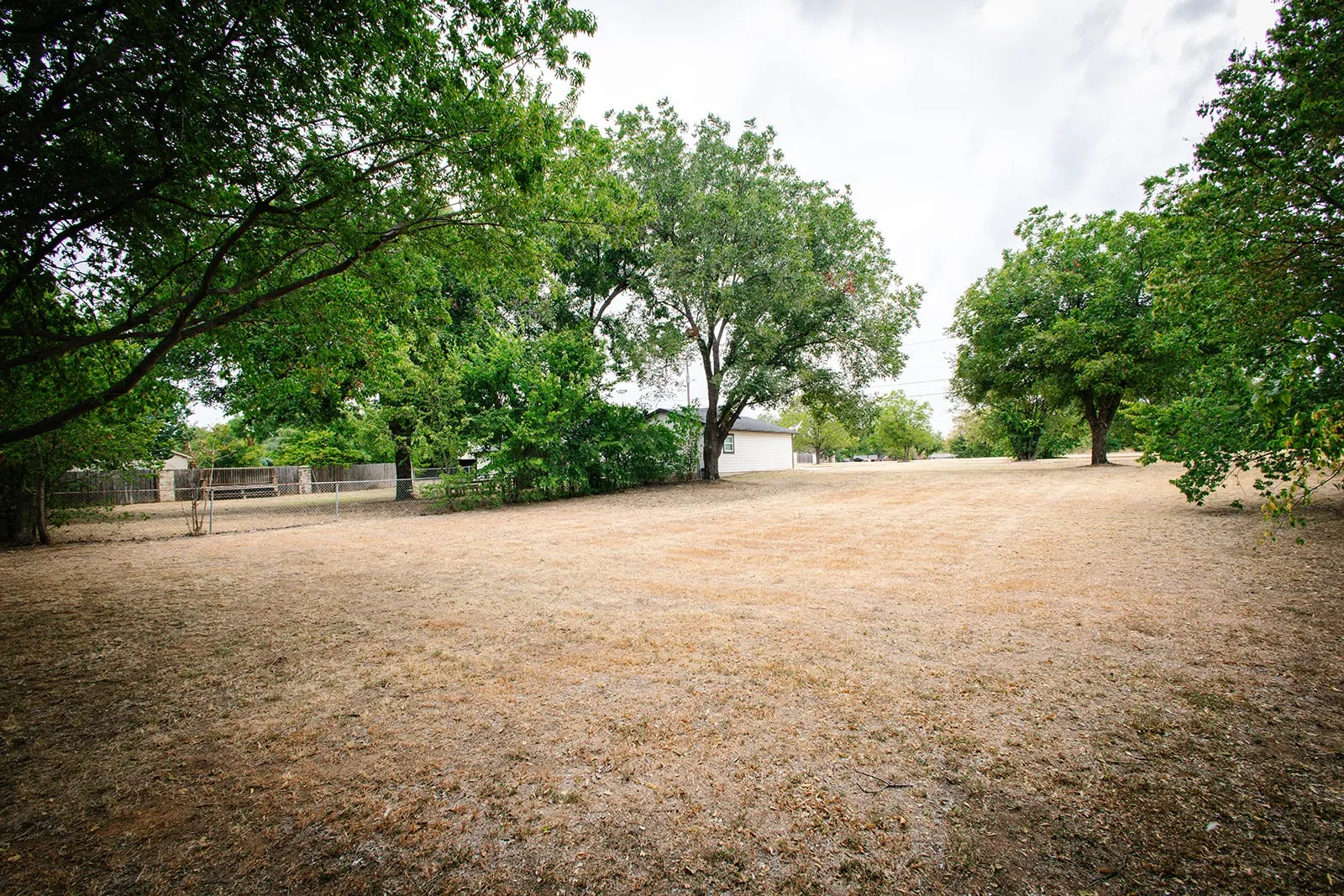 Expansive open lot featuring mature trees and a partial perimeter fence