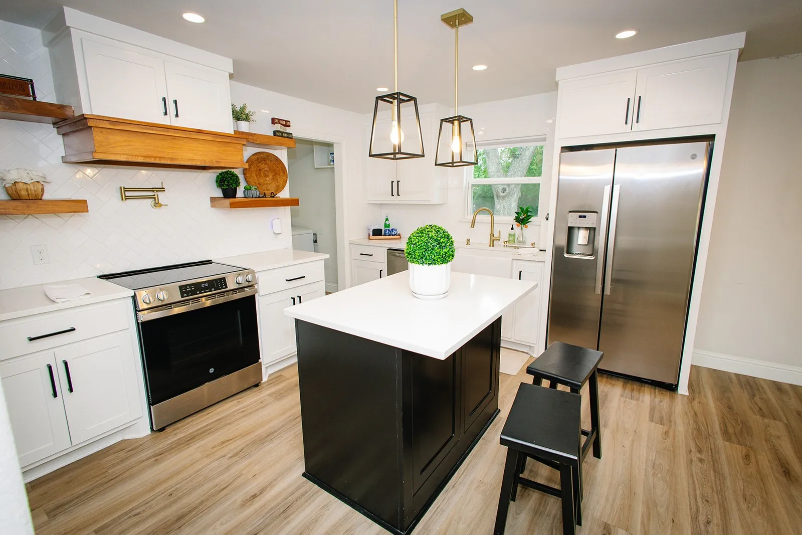 White cabinetry, stainless steel appliances, wood-finish flooring, kitchen island with contrasting base, and pendant lighting fixtures