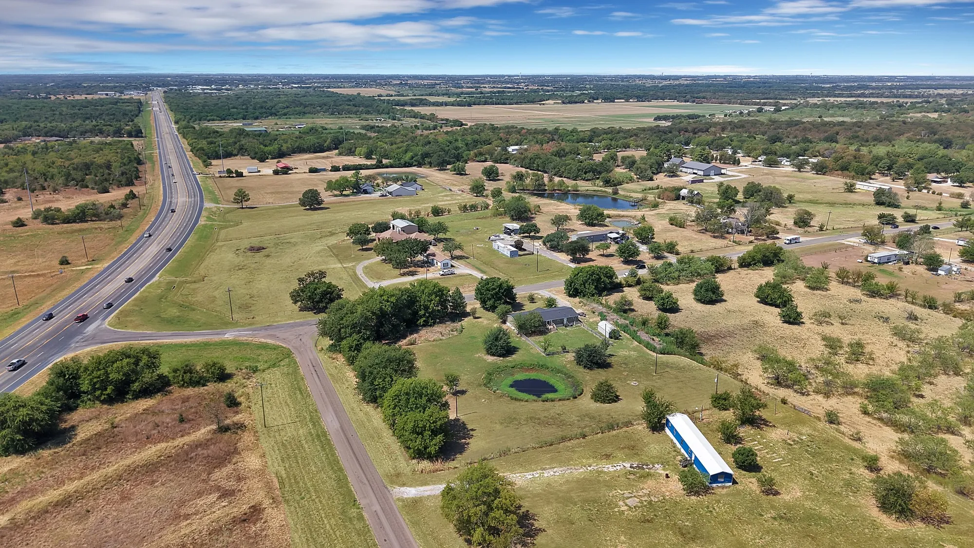 Expansive rural landscape featuring multiple structures, a pond, and direct highway access