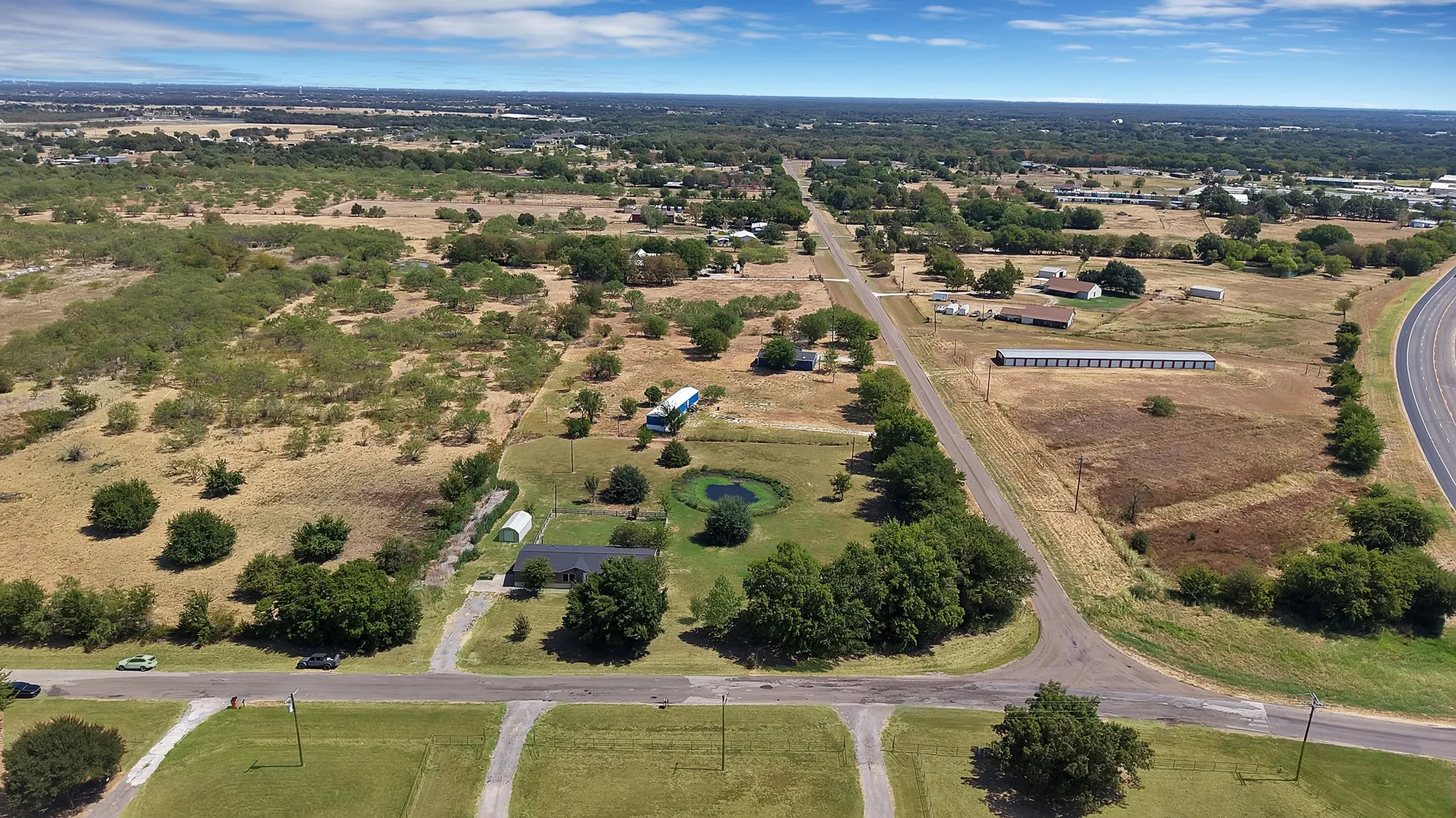 Expansive land parcel featuring open fields, scattered mature trees, and a visible roadway