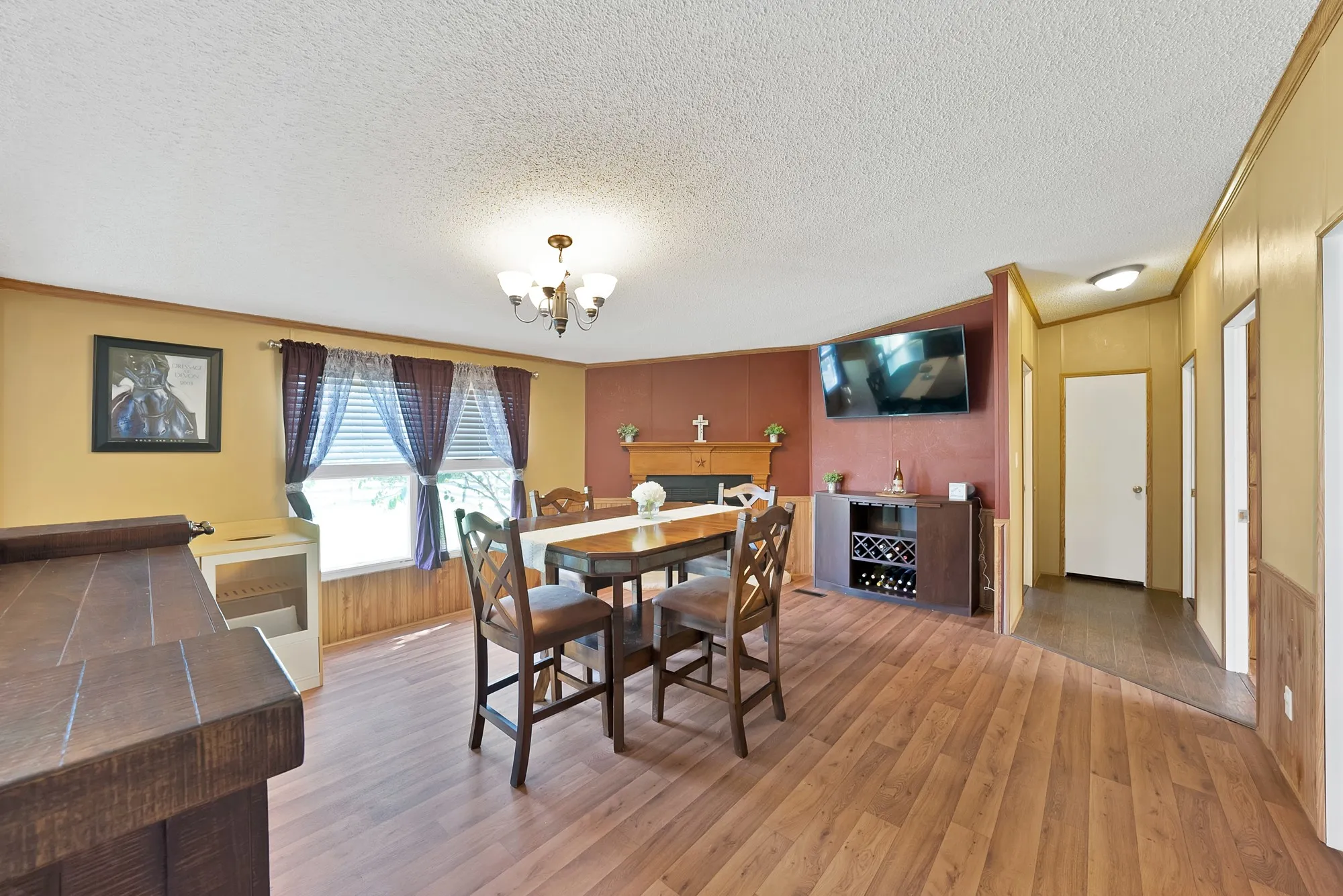 Wood-finish flooring throughout, featuring a built-in media console with wine storage, a decorative fireplace, and a ceiling-mounted chandelier