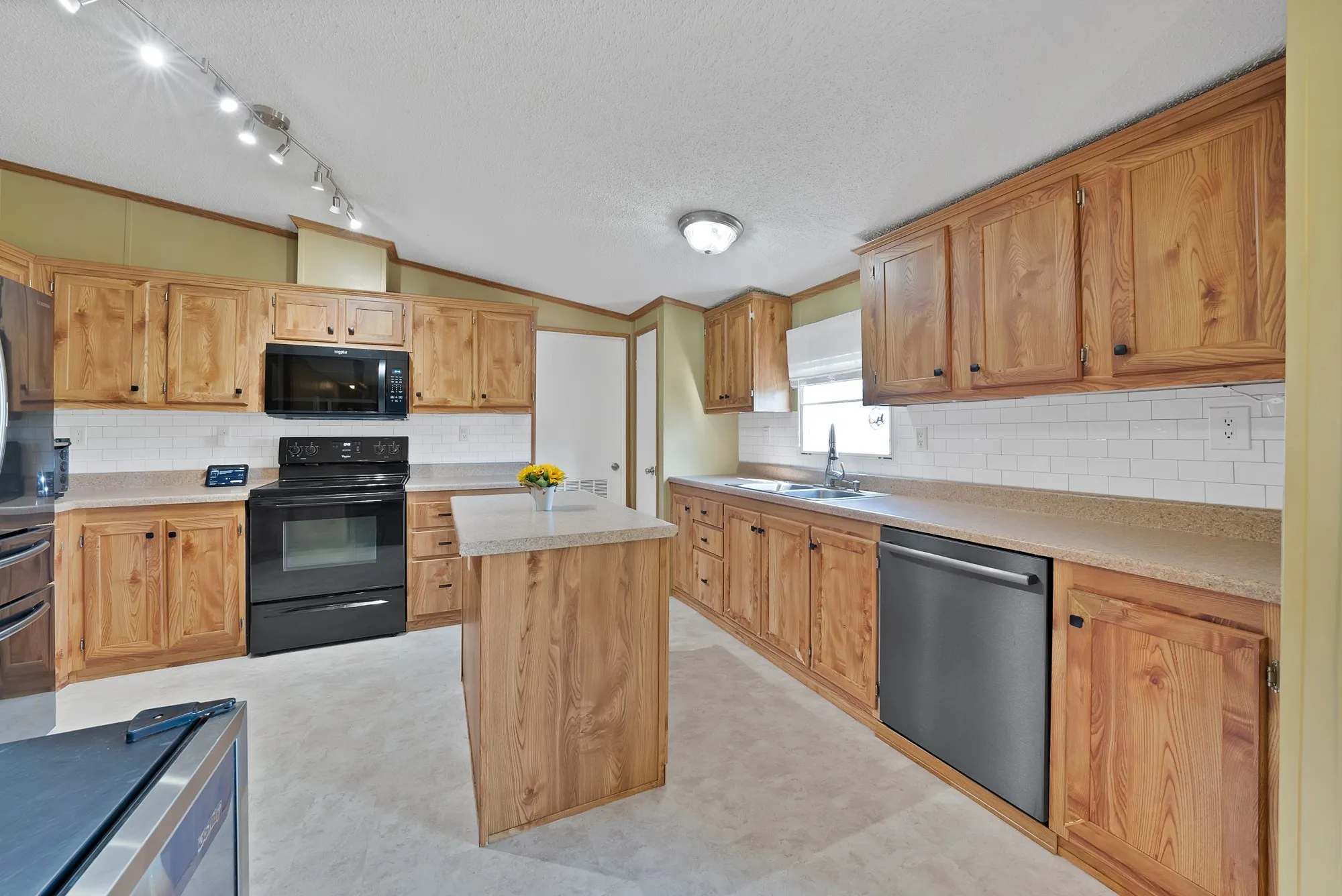 Kitchen featuring wood cabinetry, white subway tile backsplash, a central island, and black appliances