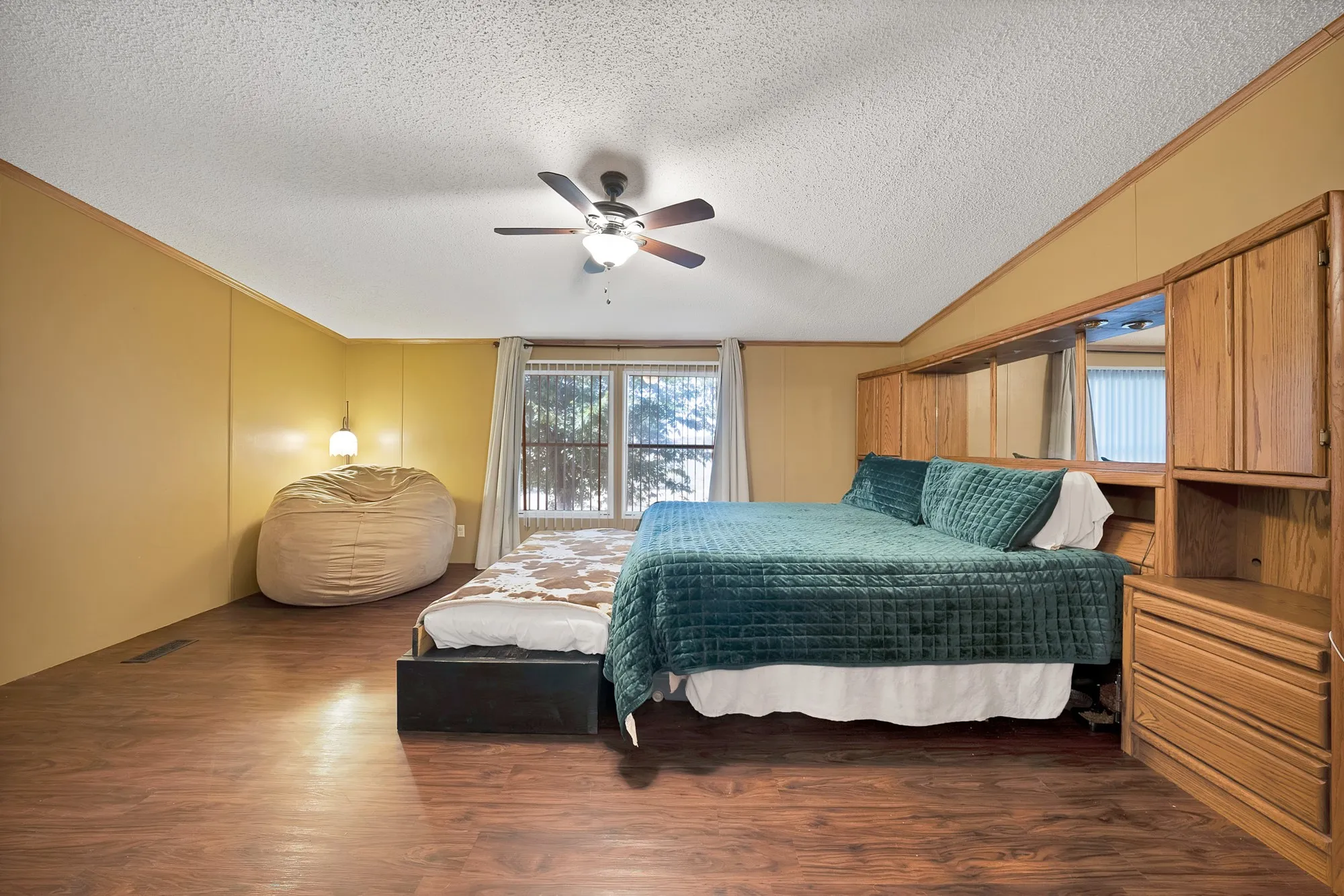 Wood-finish flooring throughout, ceiling fan with integrated lighting, built-in wooden cabinetry, and large window