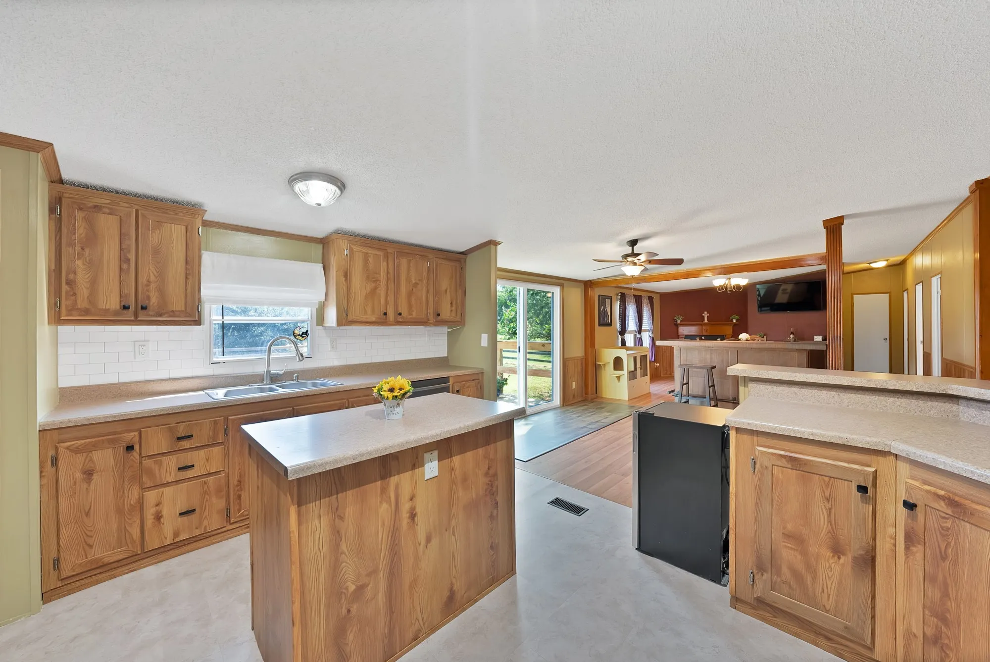 Kitchen featuring wood-finish cabinetry, light-toned countertops, a subway tile backsplash, and a central island