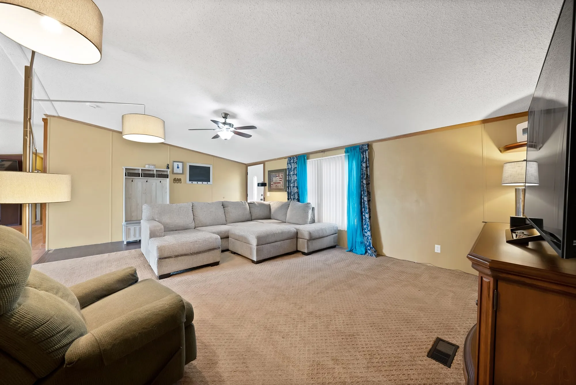 Carpeted living area with a ceiling fan, wall-mounted television, and built-in shelving