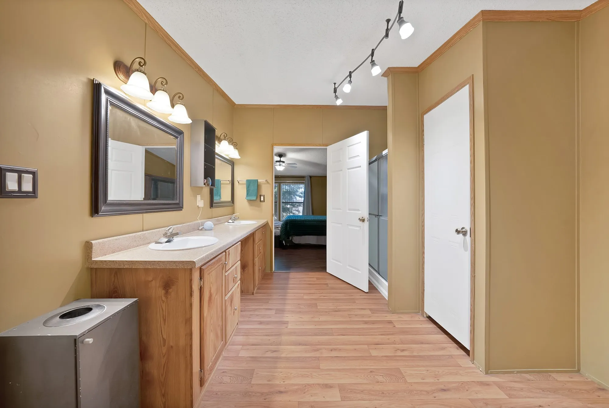 Dual vanity with wood-finish cabinetry, track lighting, and wood-finish flooring