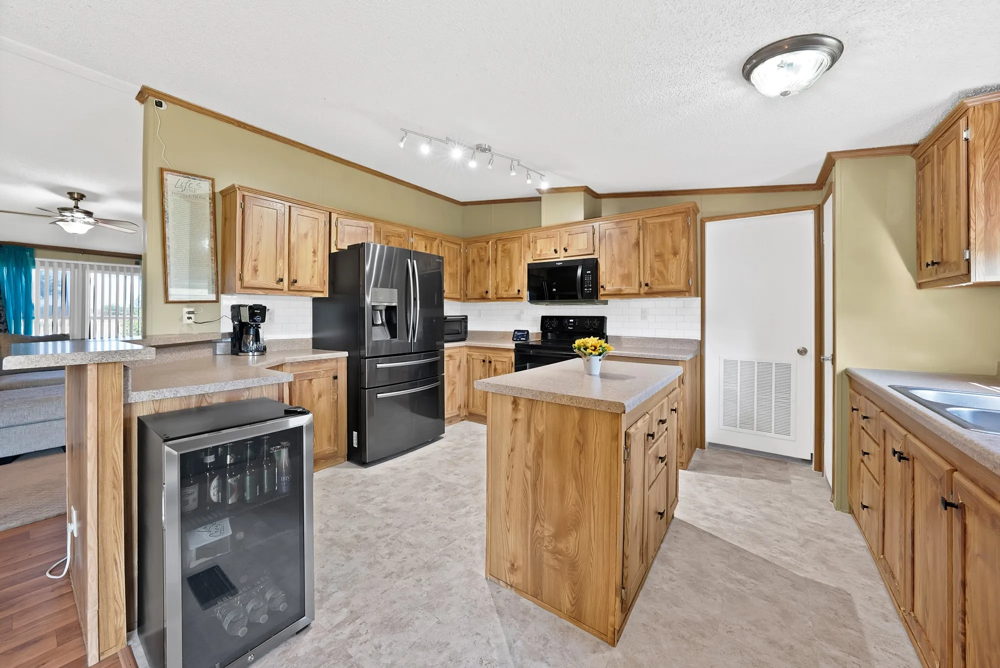 Kitchen featuring wood-finish cabinetry, black appliances, a central island, and a built-in beverage cooler