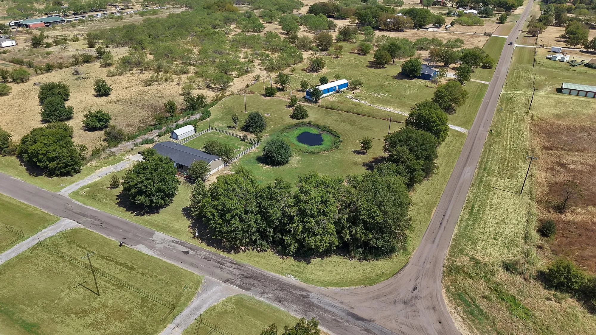 Expansive lot featuring a residential structure, mature trees, a natural pond, and accessory buildings