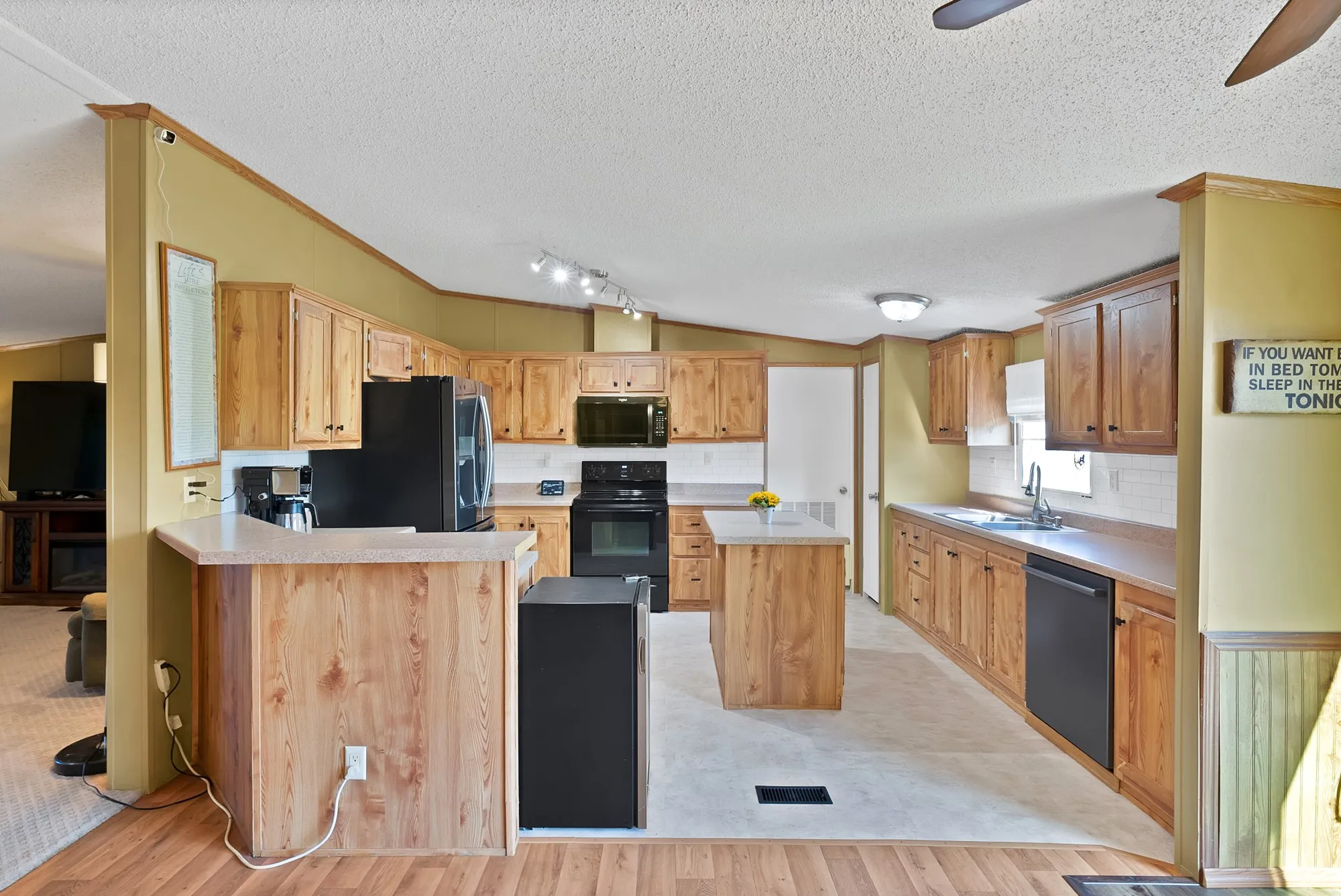 Kitchen featuring wood-finish cabinetry, a central island, black appliances, white countertops, and a tile backsplash