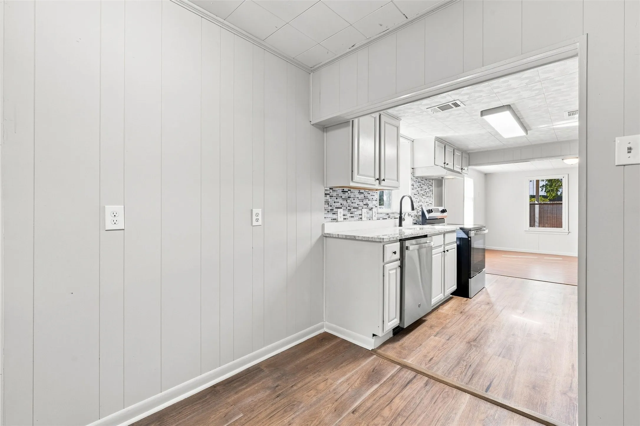 Kitchen featuring wood-finish flooring, white cabinetry, a mosaic tile backsplash, a stainless steel dishwasher, and a black range