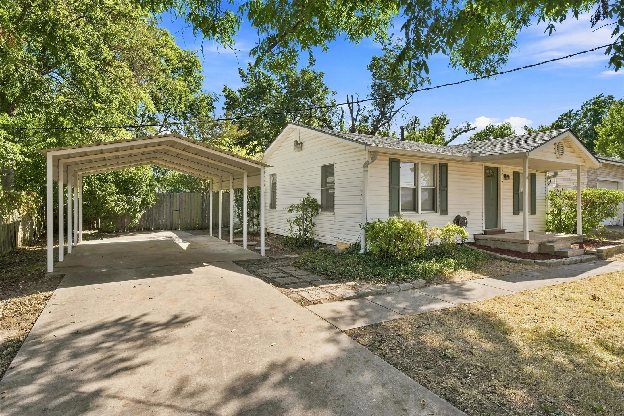 White siding exterior with a covered front porch, dark shutters, a concrete driveway, and a covered carport