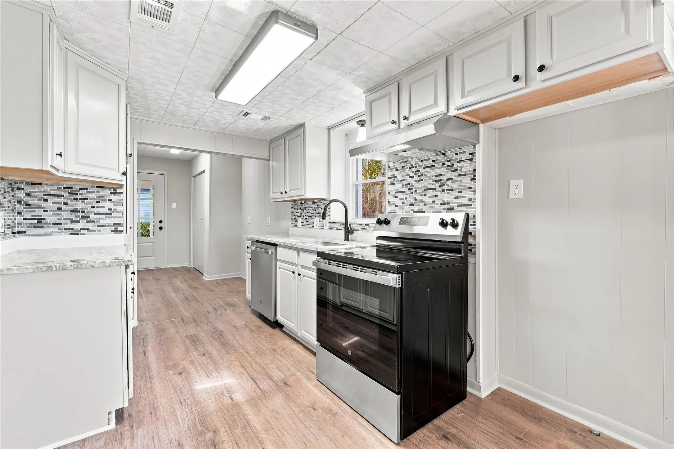 Kitchen featuring wood-finish flooring, white cabinetry, a mosaic tile backsplash, and stainless steel appliances