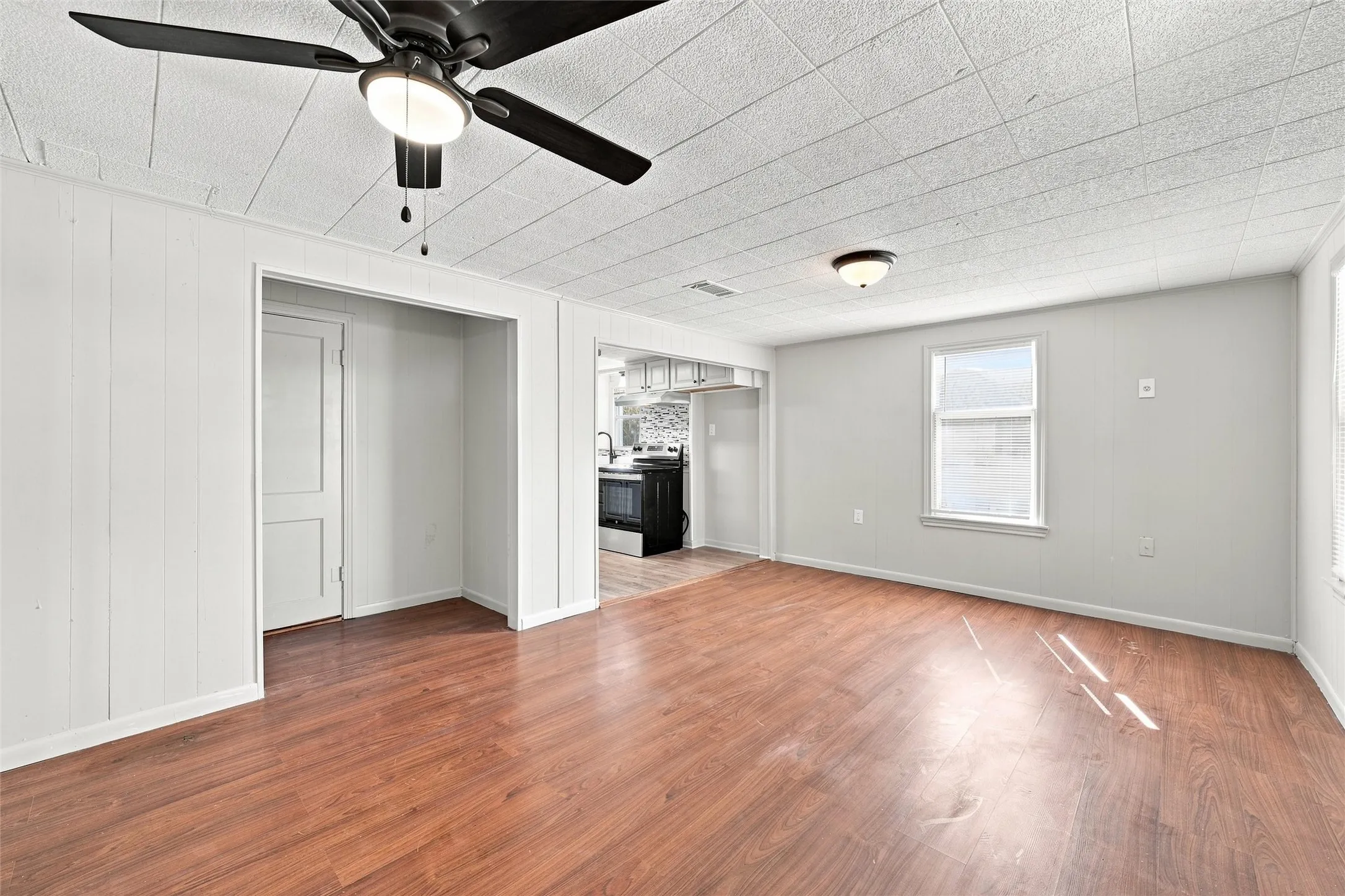 Wood-finish flooring throughout, white paneled walls, and a ceiling fan with integrated lighting