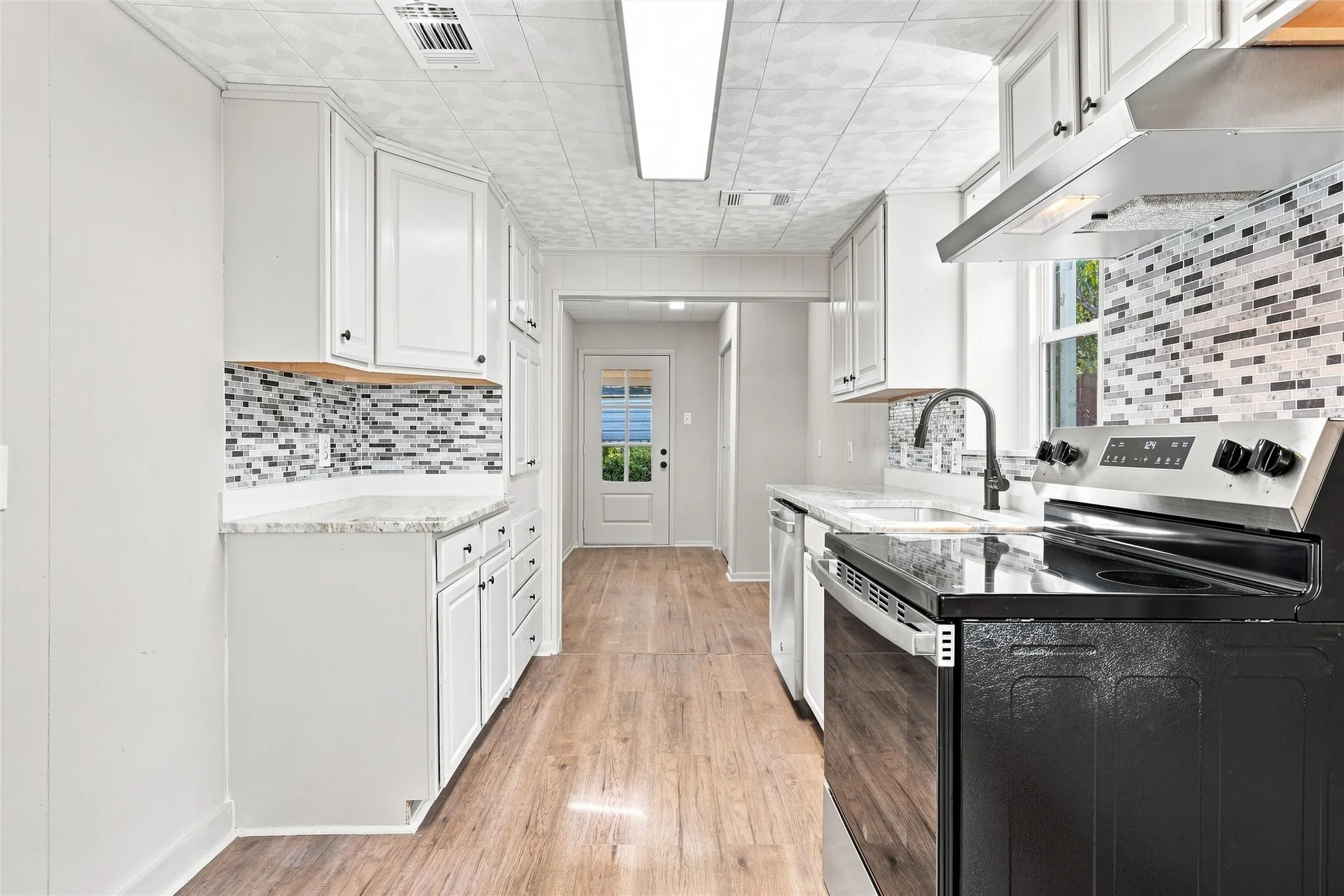 Kitchen featuring white cabinetry, a mosaic tile backsplash, black and stainless steel appliances, a black gooseneck faucet, and wood-finish flooring
