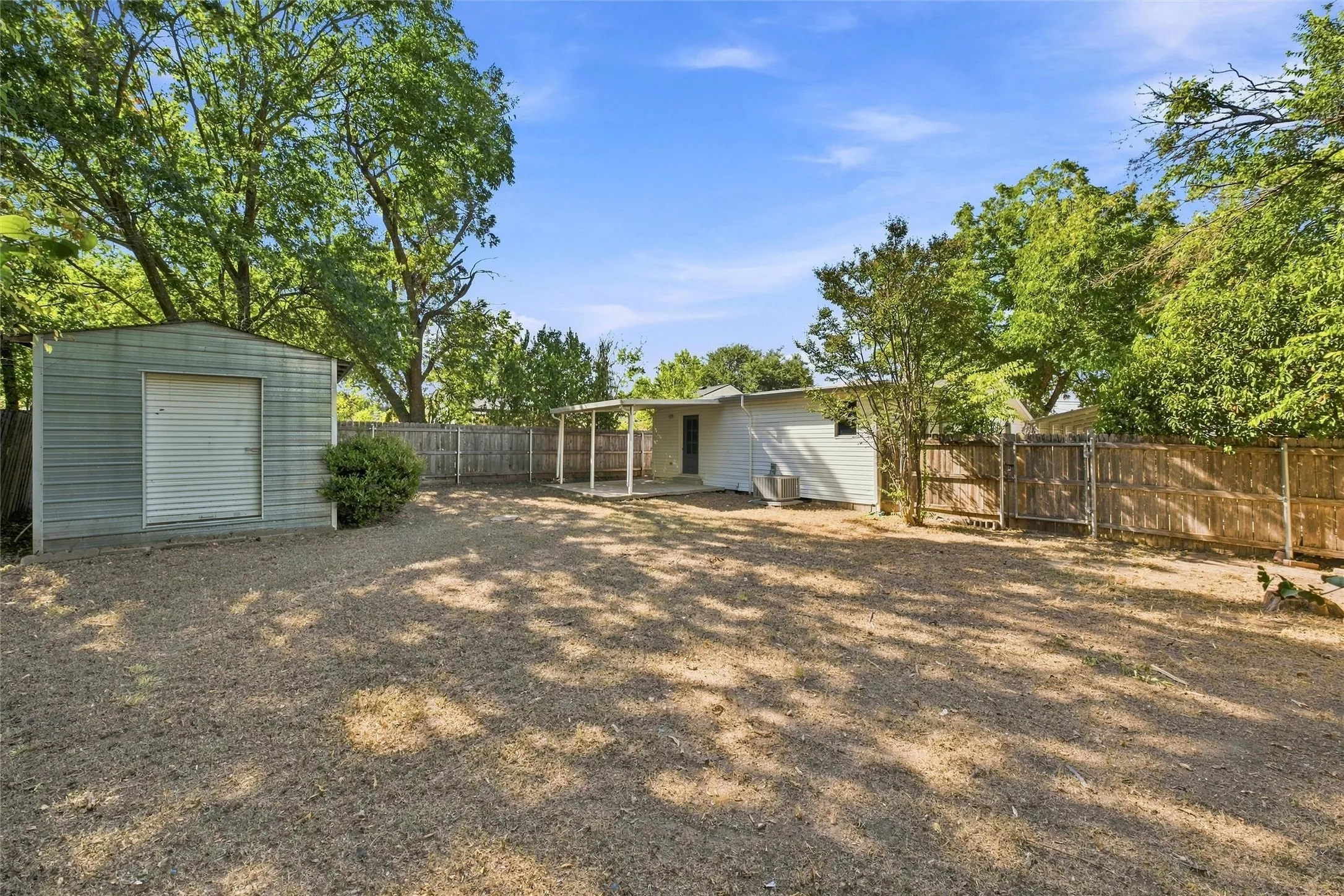 Expansive gravel yard featuring a corrugated metal shed with a roll-up door, a covered patio area, and wood privacy fencing