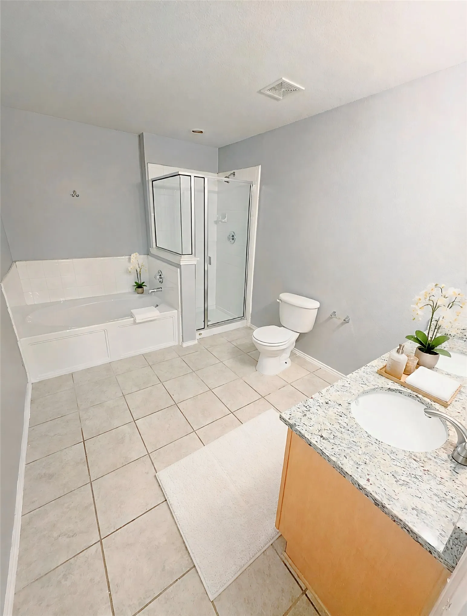 Integrated soaking tub and separate glass-enclosed shower, Dual sink with a granite countertop, neutral tile flooring, new faucets.