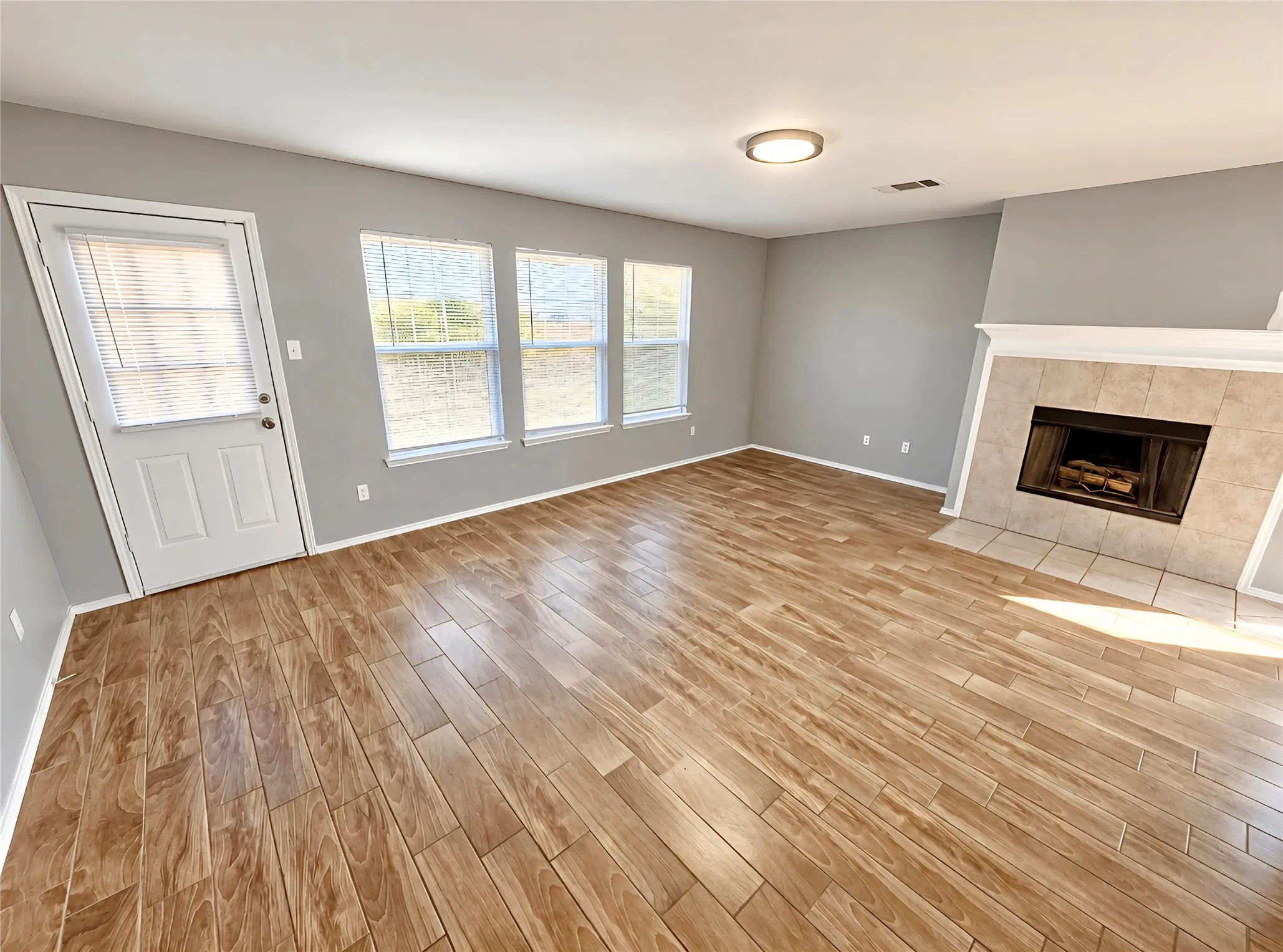 Wood-like tile flooring, multiple windows, a tile-surround fireplace with a white mantel, and bright lighting.
