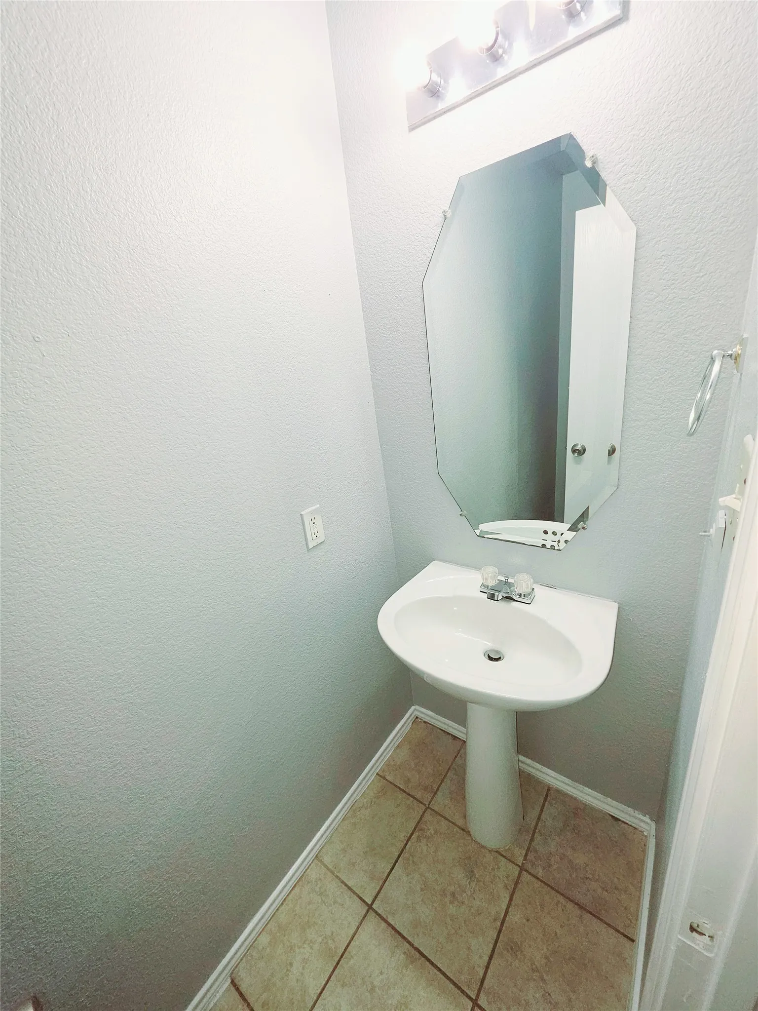 Pedestal sink, wall mirror, overhead vanity lighting, and ceramic tile flooring