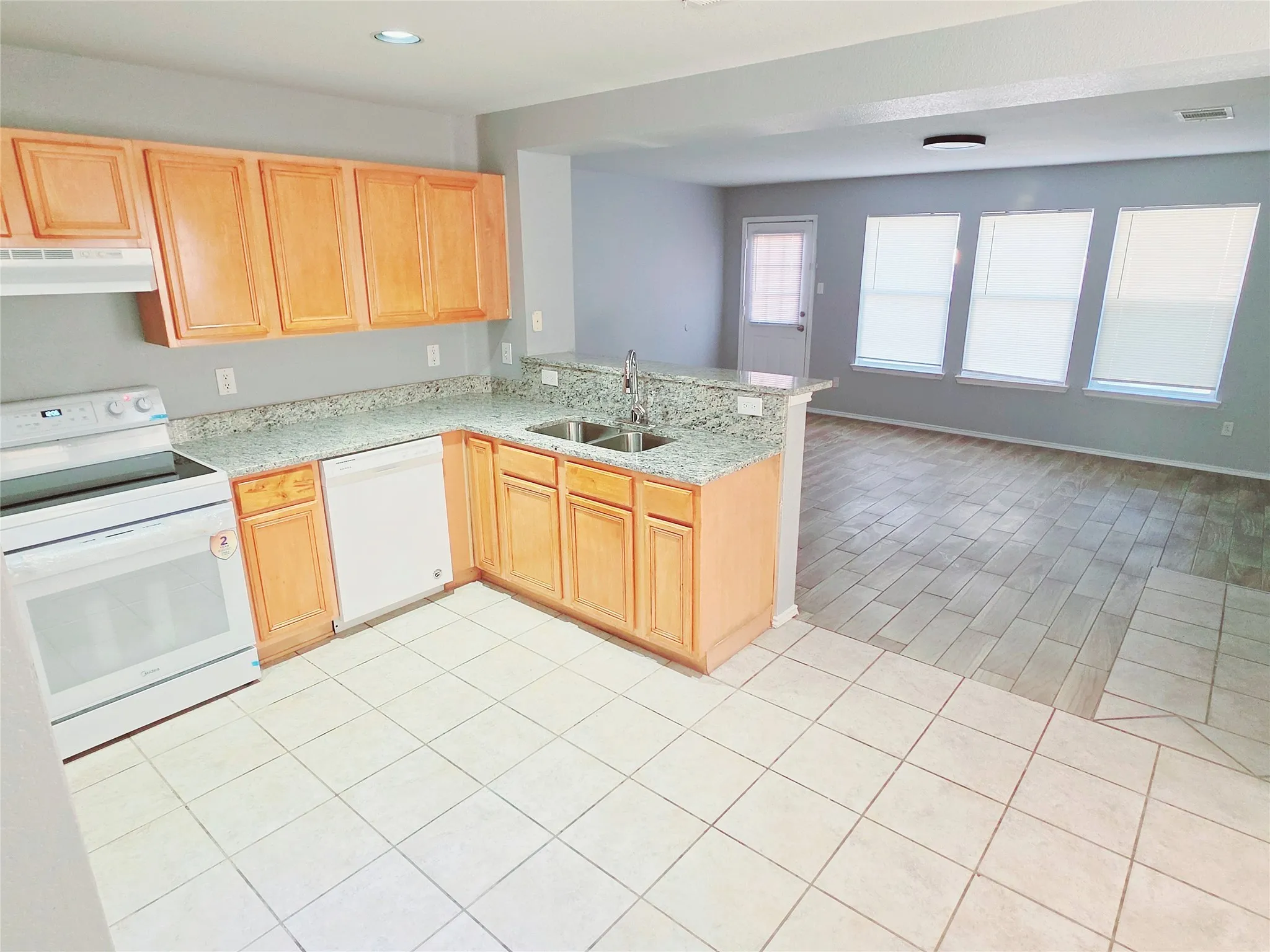 Kitchen with wood-finish cabinetry, light-toned granite countertops, and dual basin sink