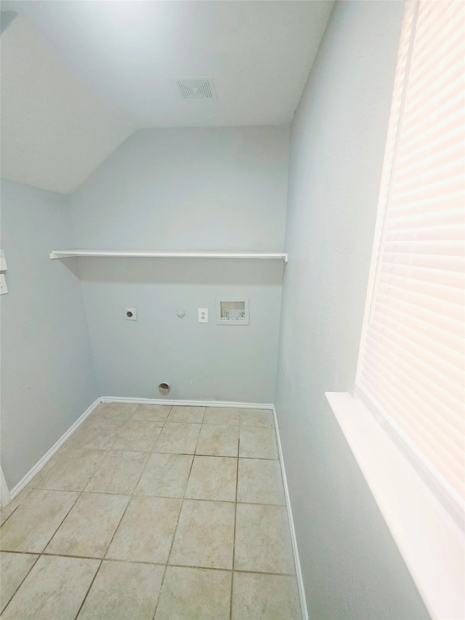 Laundry area featuring tile flooring, a built-in white shelf, and a window with blinds