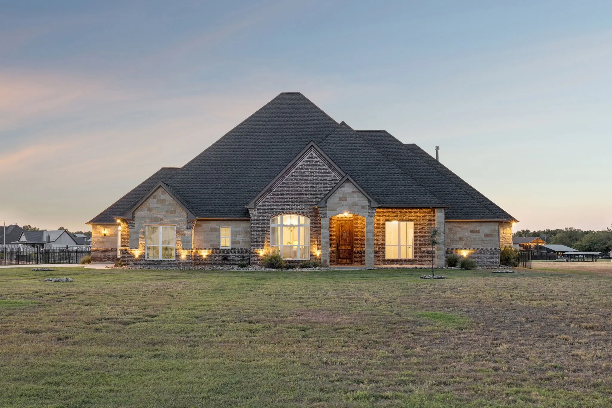 Stone and brick exterior with a multi-level roofline, arched entry, and extensive landscape lighting