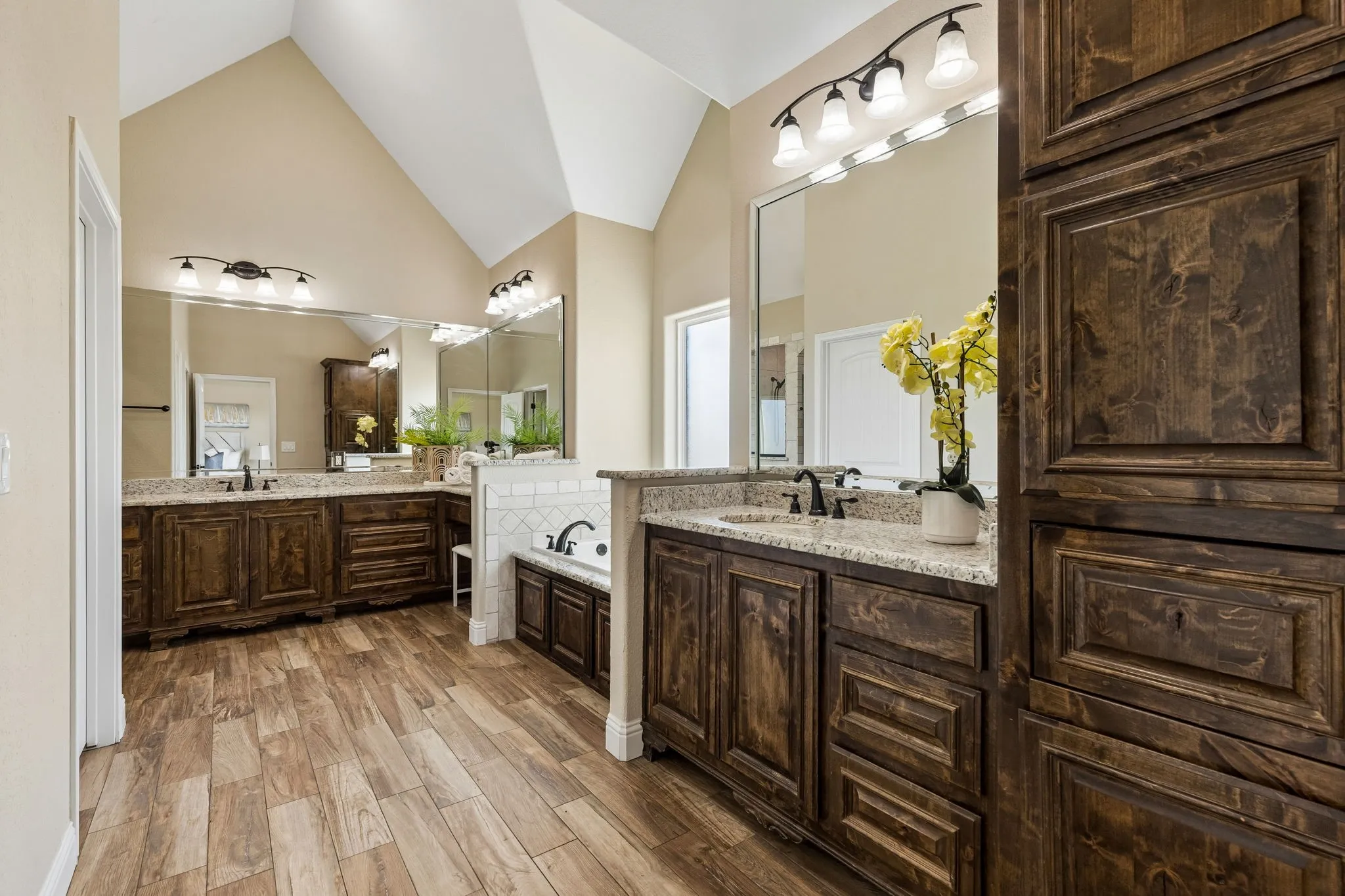Vaulted ceiling, wood-finish flooring, dual vanities with granite countertops, built-in soaking tub, and extensive wood cabinetry