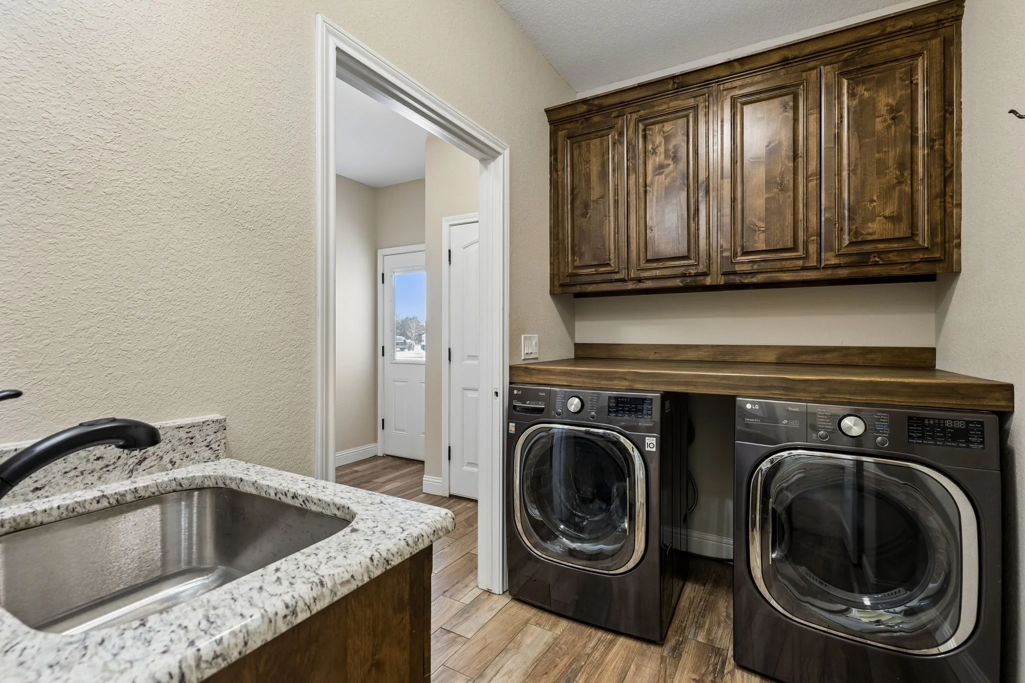 Laundry area featuring wood-finish flooring, a utility sink with a stone-finish countertop, and wood cabinetry